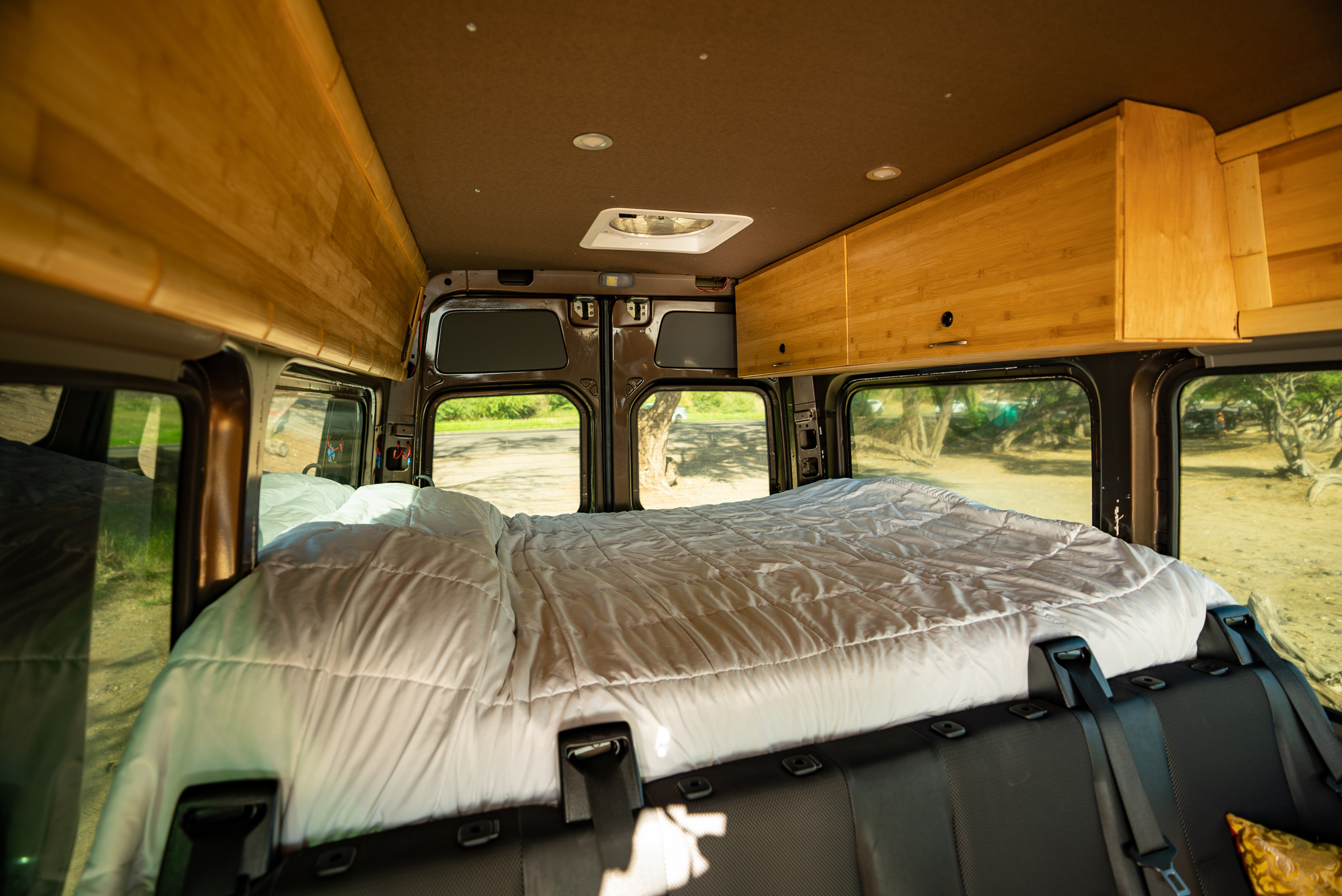 Inside this cozy RV rental: a plush camper van bedroom with built-in wooden storage & scenic window views.. Mercedes-Benz Sprinter 2015