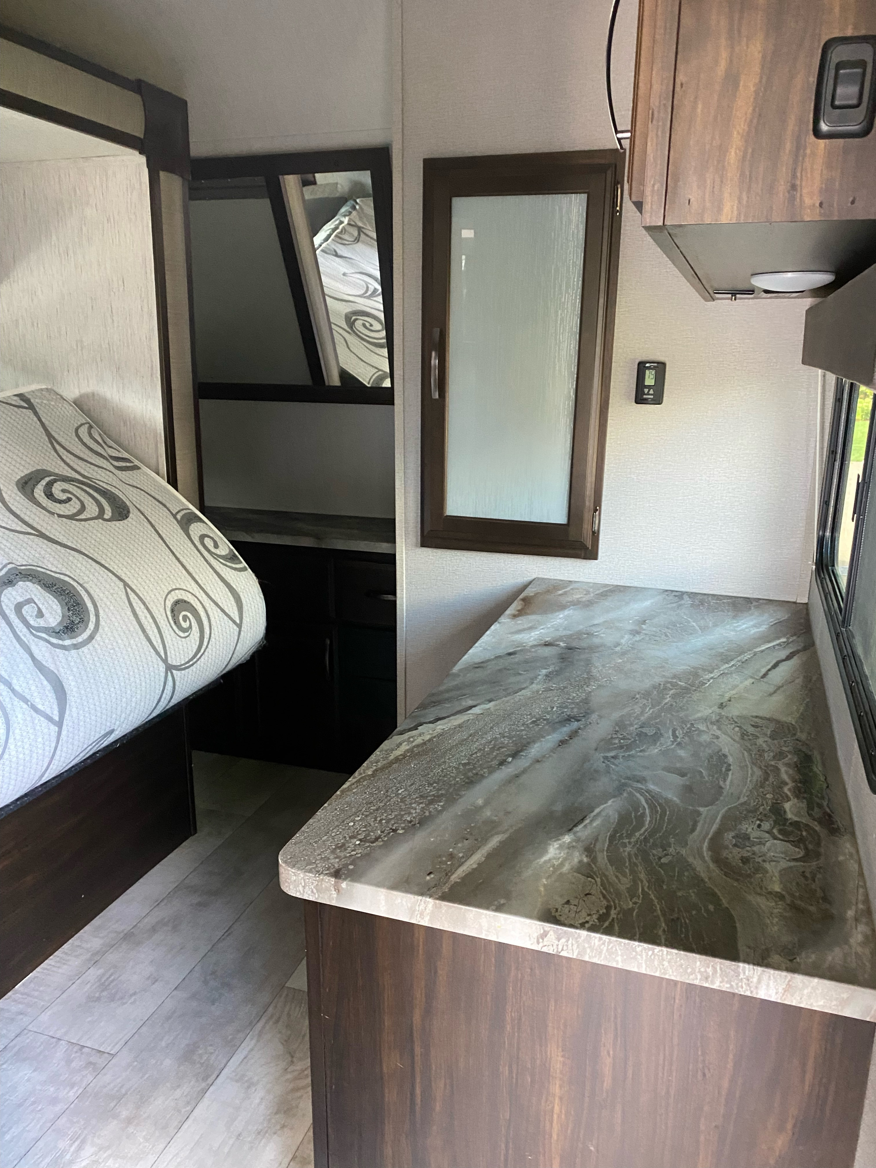 RV rental interior featuring a cozy bed, sleek marbled counter, storage, and modern amenities like a thermostat.. Grand Design Momentum 2020
