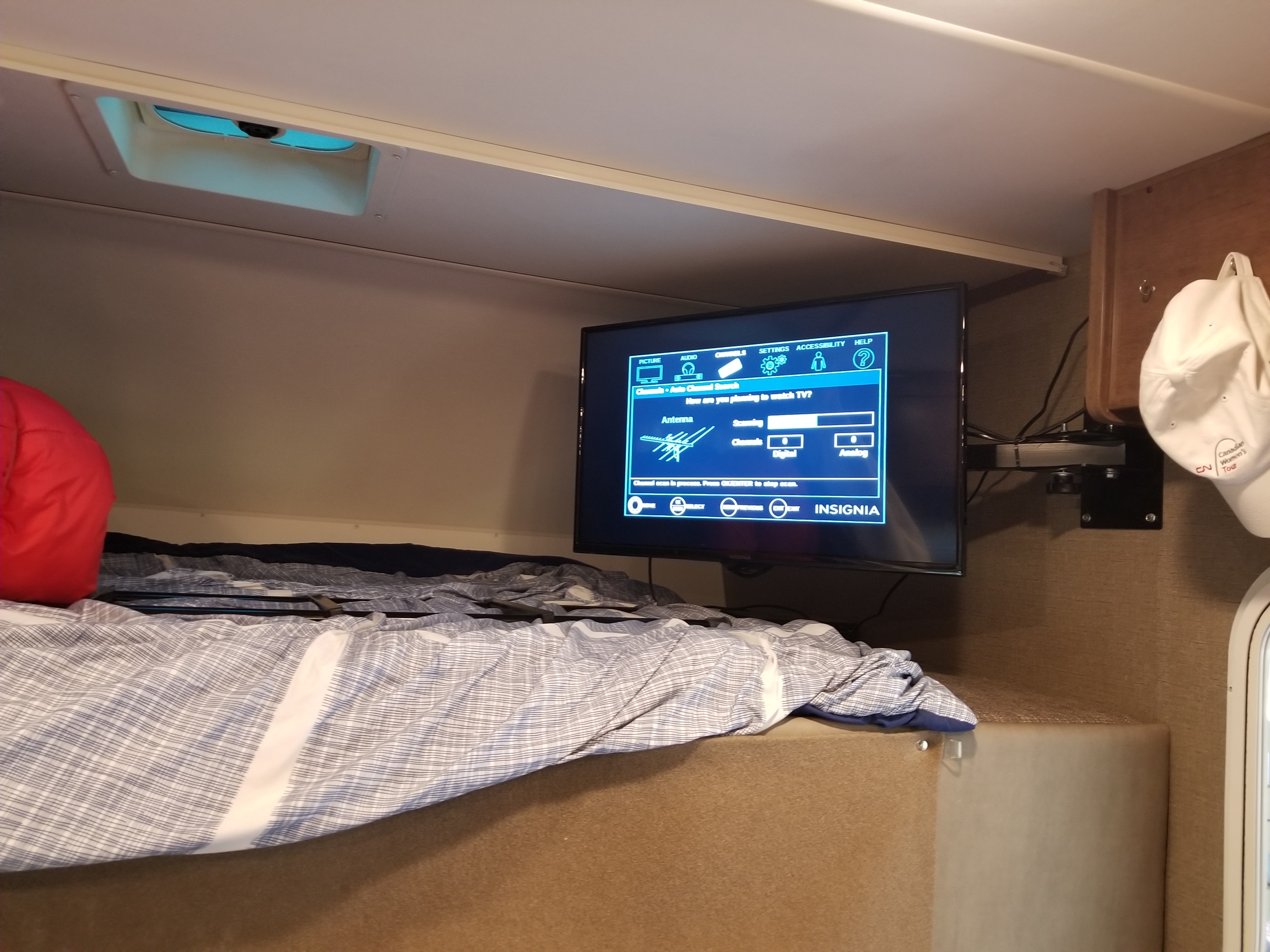 RV rental interior features a bed, and a mounted Insignia TV searching for channels, offering entertainment on the go.. Winnebago Outlook 2019