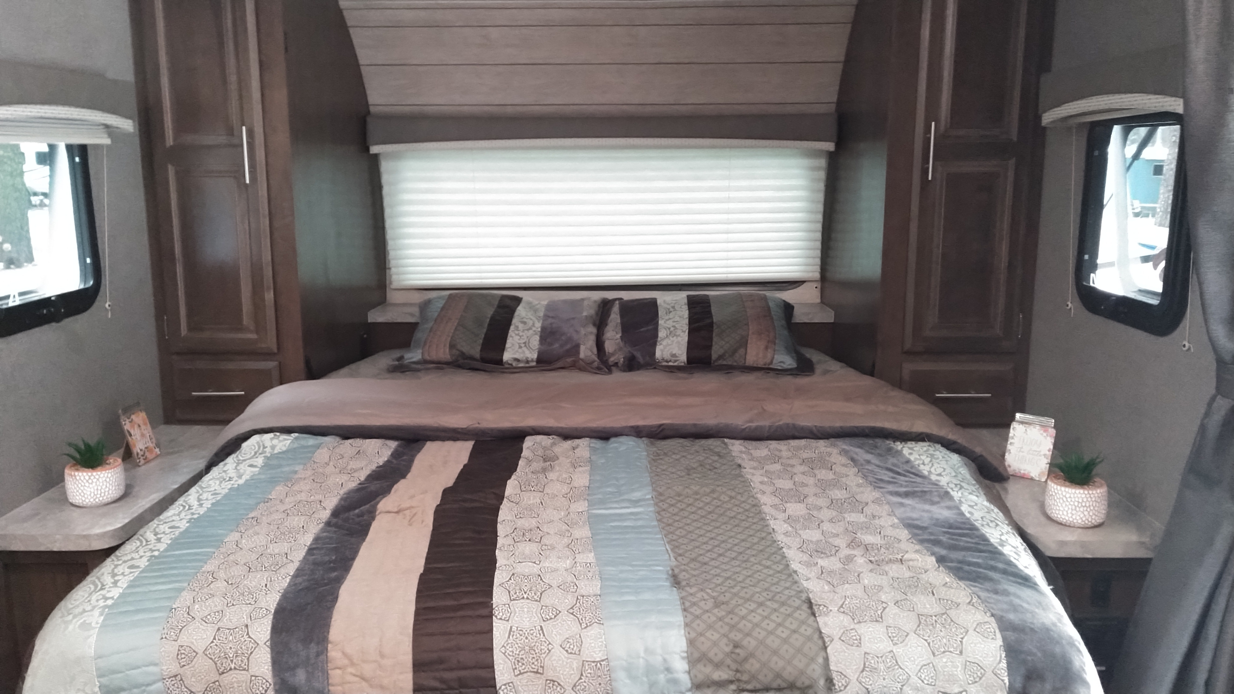 Cozy RV rental bedroom features a striped comforter, accent pillows, side windows, and ample storage for comfortable travel.. Forest River Rockwood Mini Lite 2020