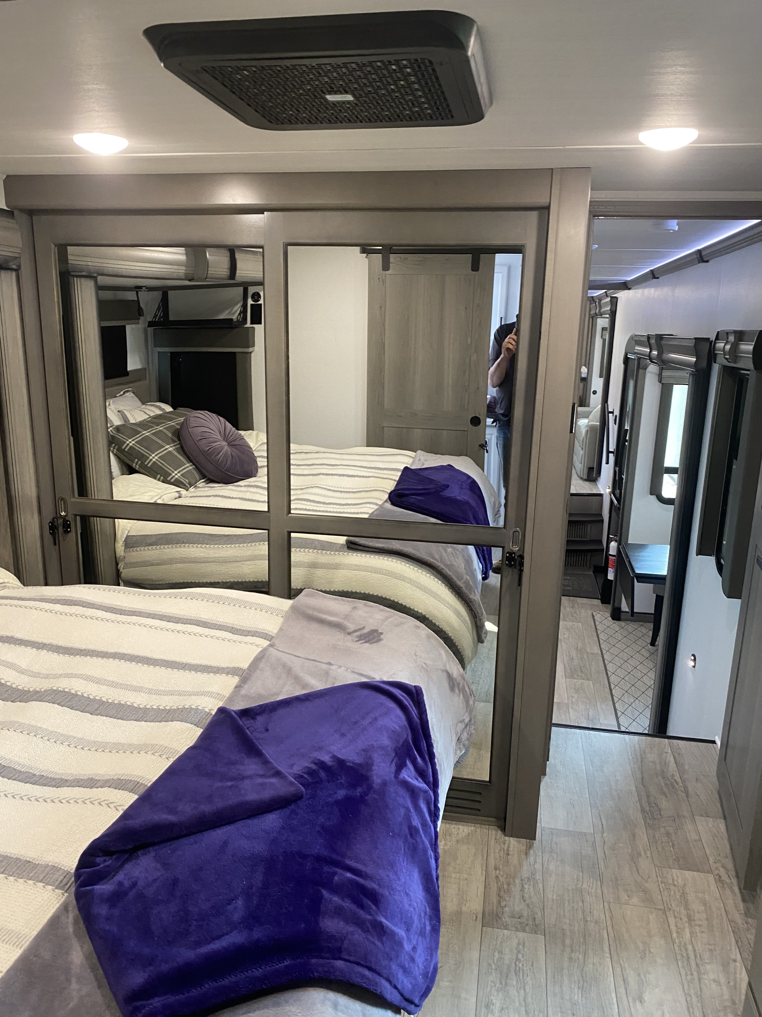 Step inside this modern RV rental's cozy bedroom, featuring a large mirrored closet reflecting the soft bed and purple blanket. Leads to living space.. Keystone RV Montana 2022