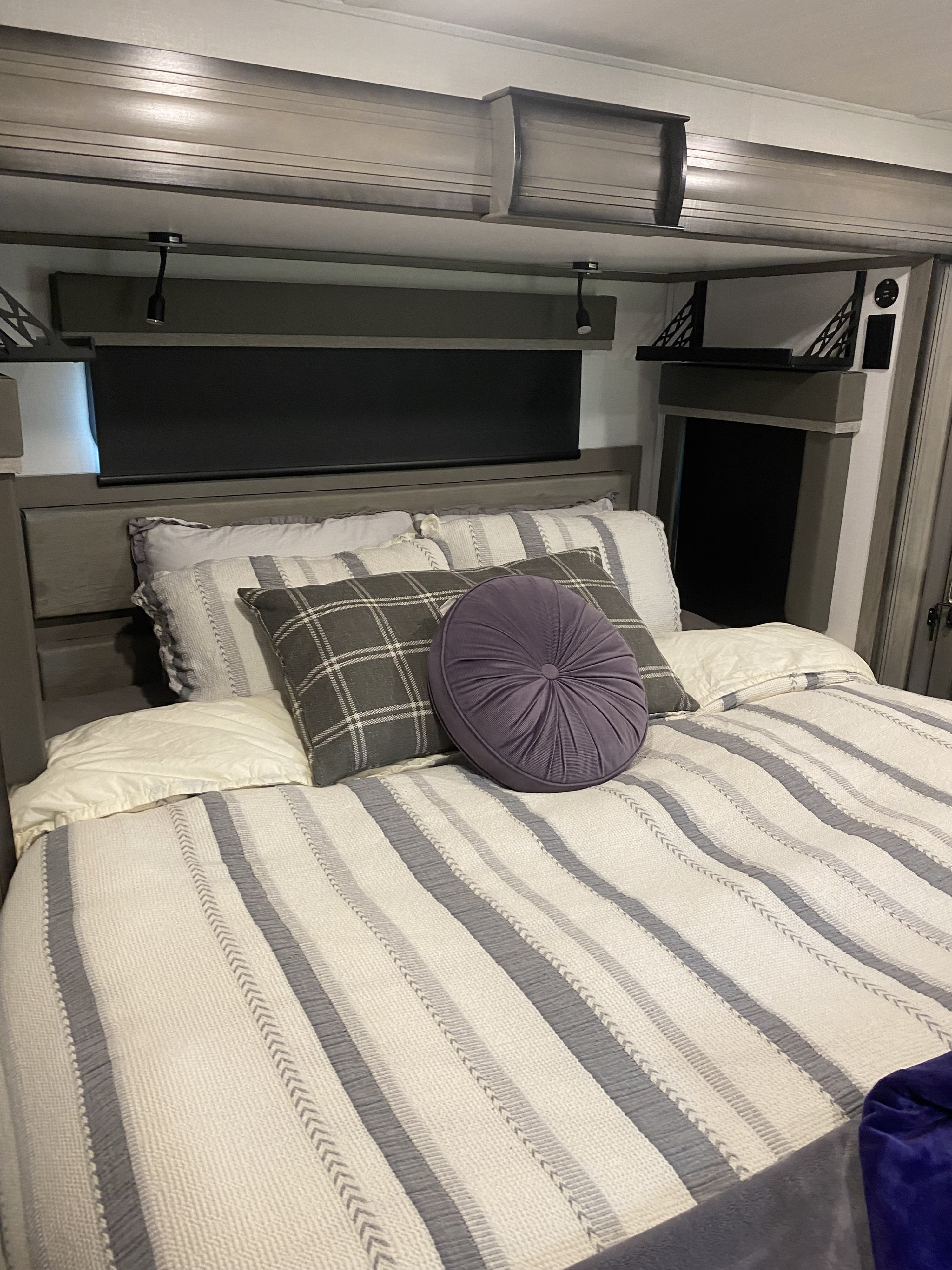 Comfortable RV rental bedroom with striped bedding, plush pillows, and built-in reading lights above the bed. Compact travel living.. Keystone RV Montana 2022