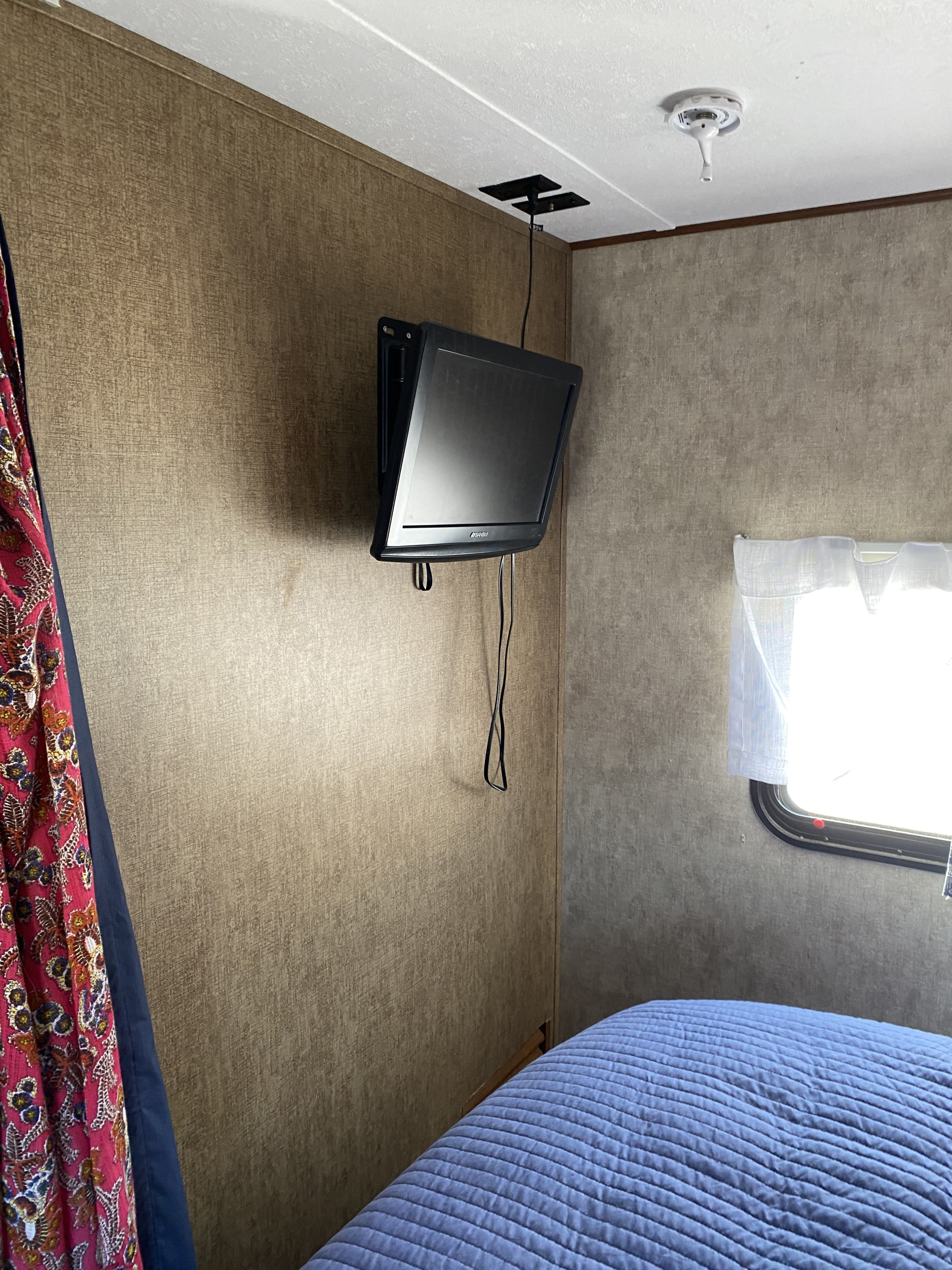 RV rental: Cozy bedroom interior featuring a wall-mounted TV, blue quilted bed, and window. Ideal for compact living.. Prime Time Avenger ATI 21RB 2015