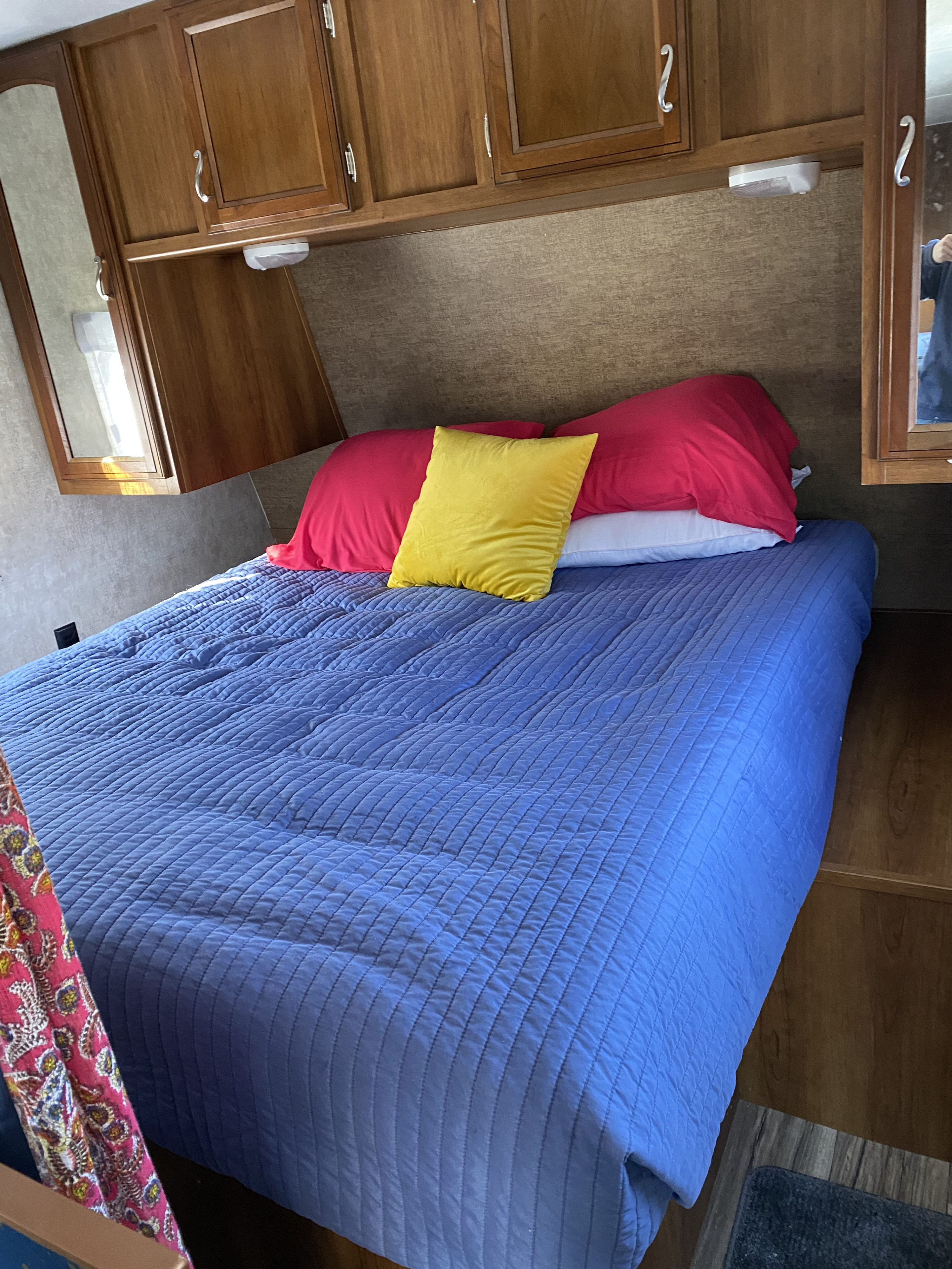 Cozy RV rental bedroom with a blue bed, colorful pillows, and overhead storage cabinets.. Prime Time Avenger ATI 21RB 2015