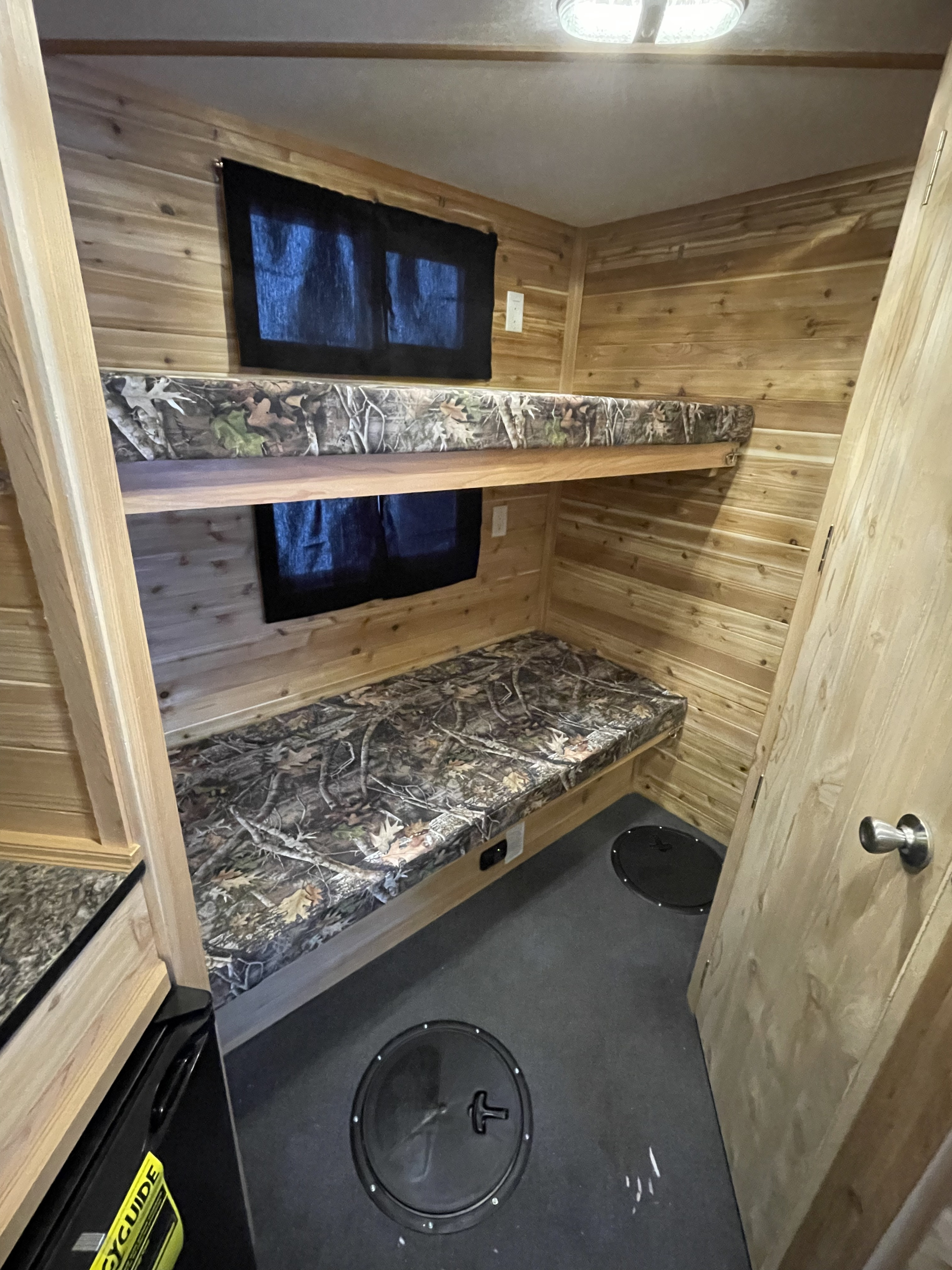 This RV rental ice fishing cabin interior features wooden walls, cozy bunk beds, and floor fishing holes.. Ice Castle Fish Houses Walleye Tracker 2023