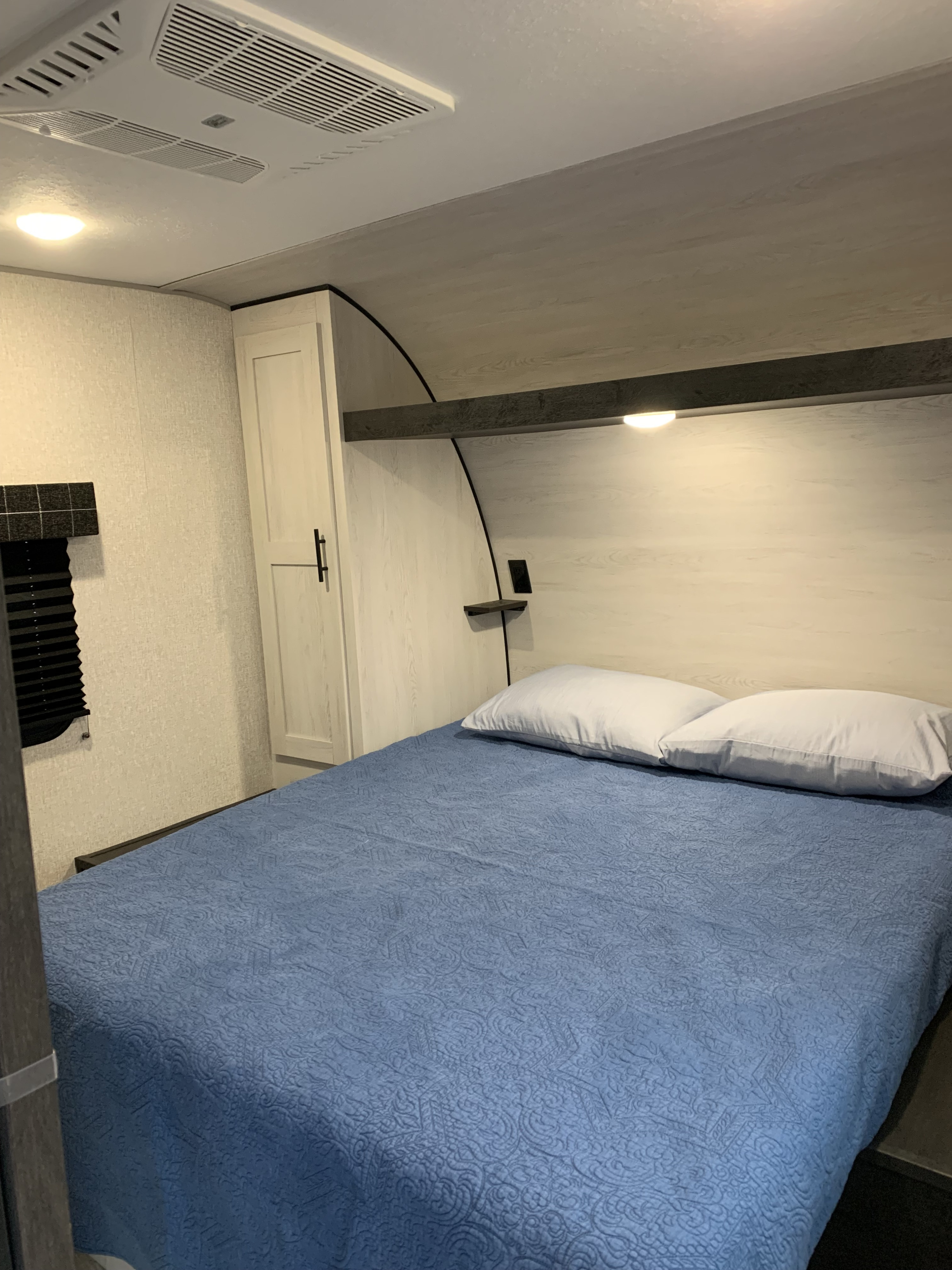 Discover a cozy RV rental bedroom: comfy bed with blue quilt, white pillows, built-in storage, and ceiling AC unit.. KZ Sportsman SE 2022
