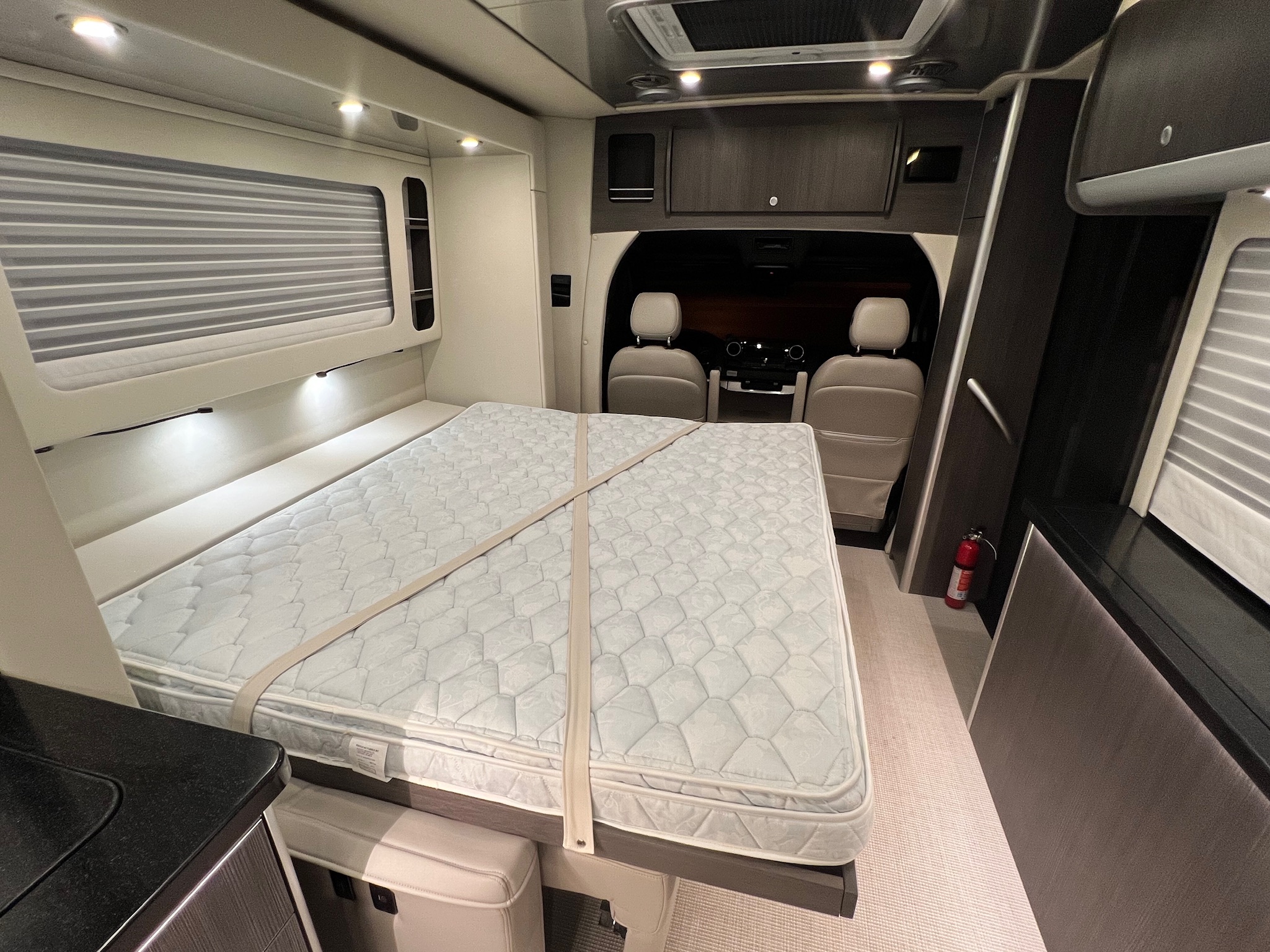 Interior of an RV rental showing a large mattress secured with straps, integrated storage, and the vehicle's cockpit.. Mercedes-Benz Atlas Airstream 2021