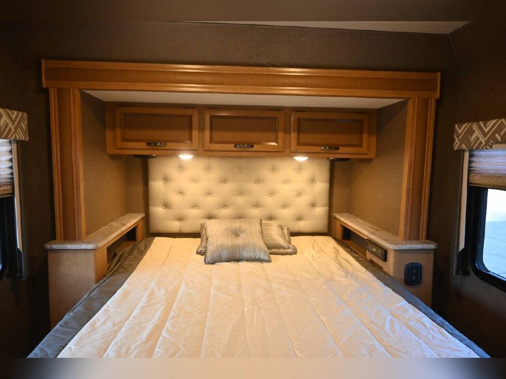 Comfortable RV rental bedroom with a plush tufted headboard, overhead cabinets, and side storage shelves.. Thor Axis 2017