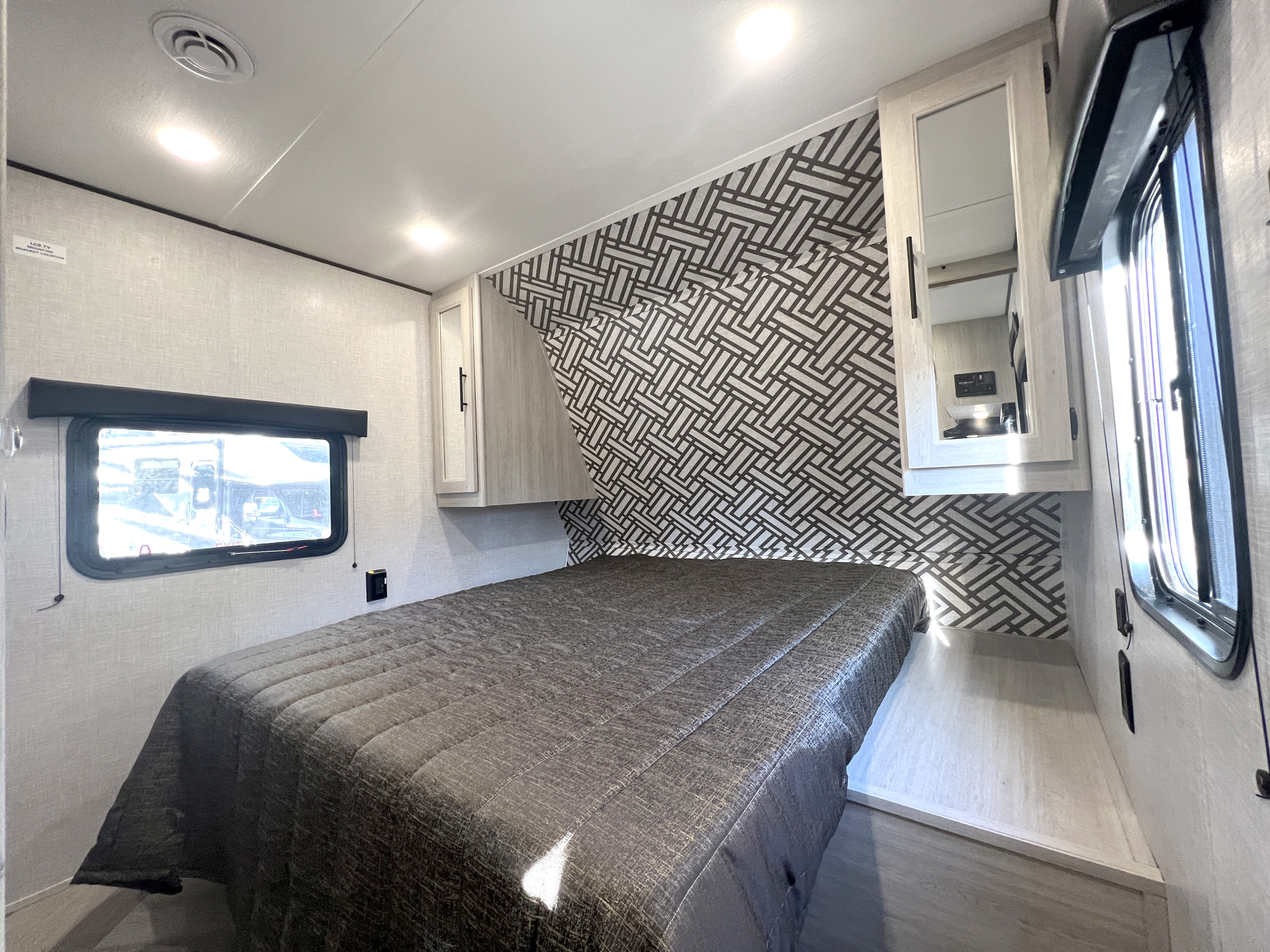 Compact RV rental bedroom with a modern bed, geometric accent wall, and windows. A cozy and functional sleeping space.. Crossroads Zinger 2023