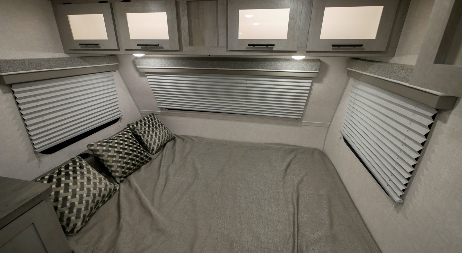 Comfortable RV rental bedroom featuring a bed, multiple windows with closed blinds, and overhead storage cabinets.. Ibex 19QHT 2022