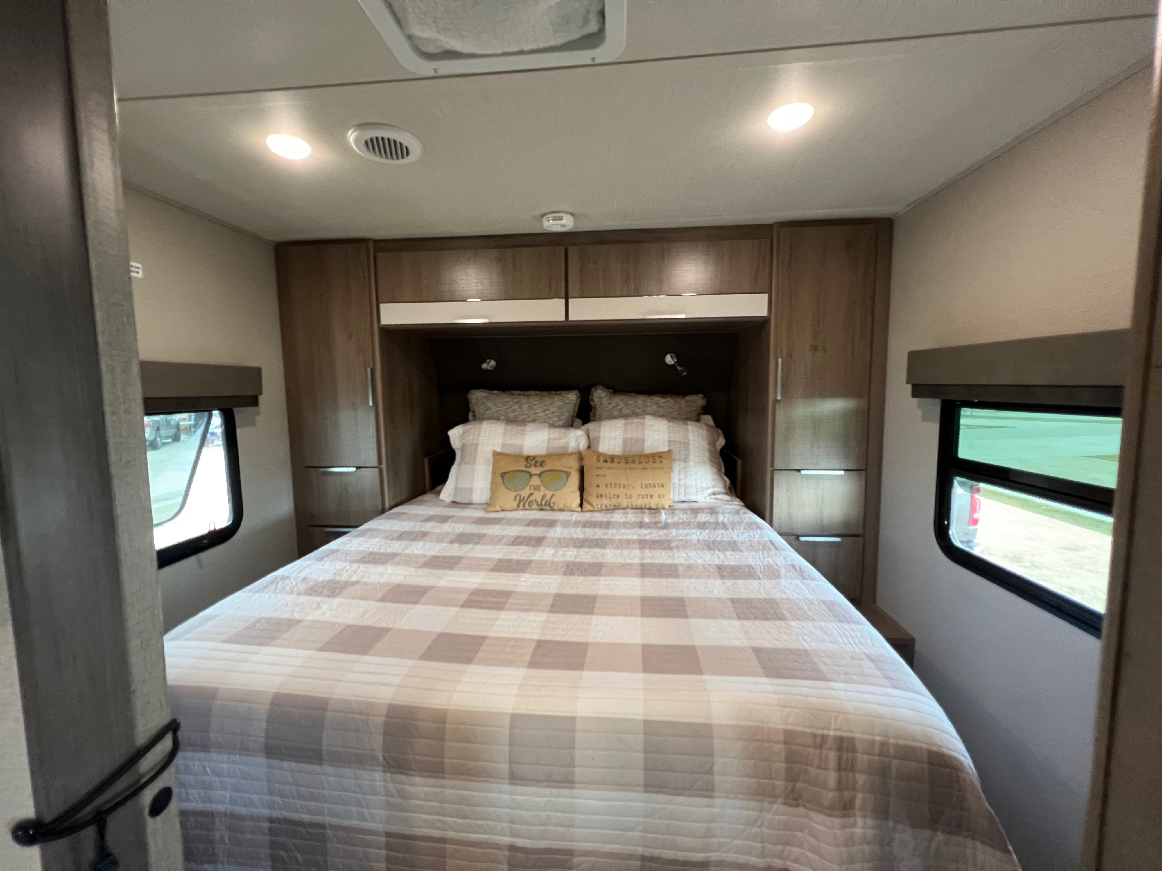 Cozy RV rental bedroom with plaid bedding, overhead cabinets, and windows for a comfortable travel experience.. Grand Design Imagine XLS 2022