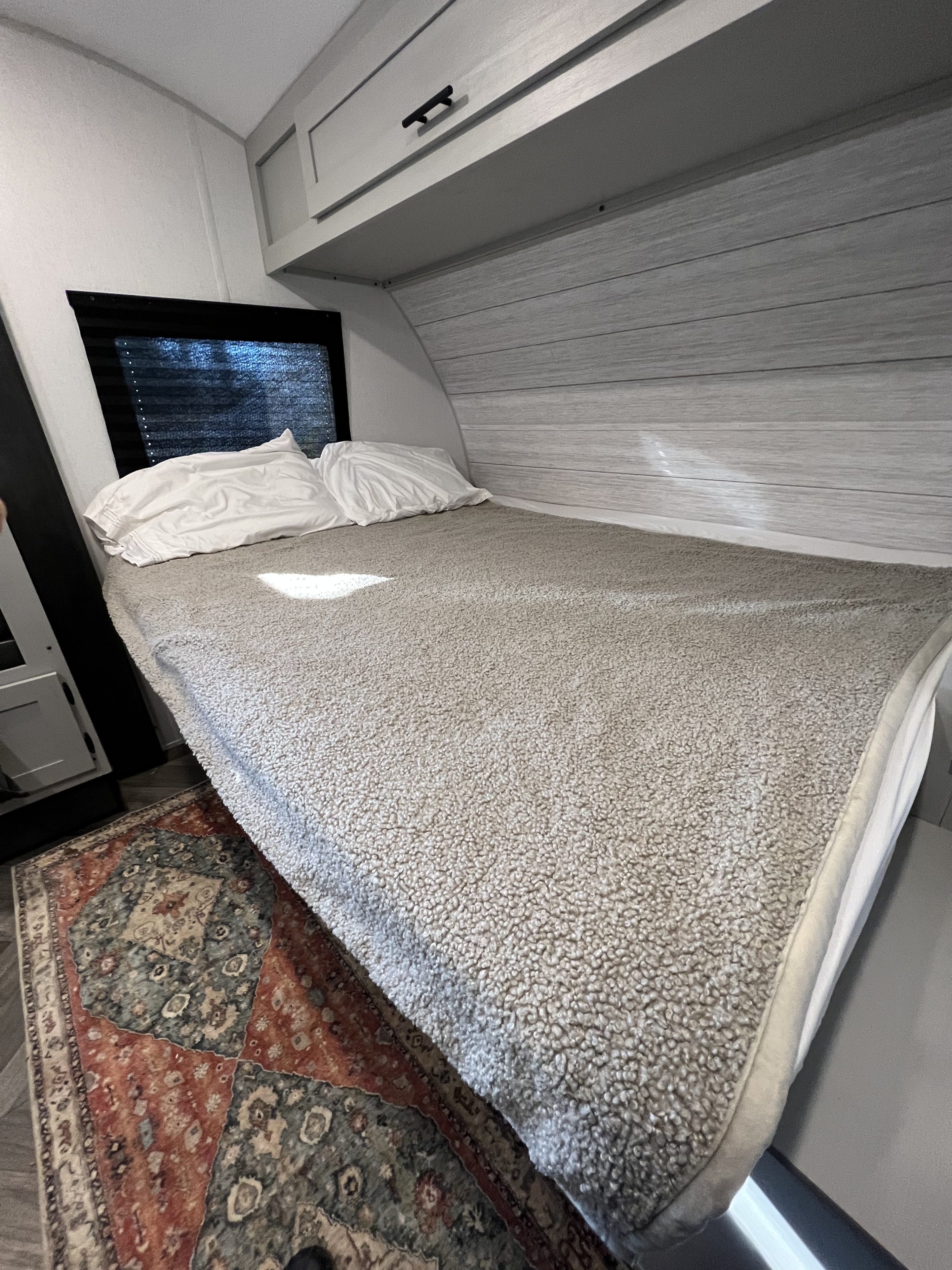 Cozy RV rental bedroom with a plush grey blanket, white pillows, and a colorful patterned rug. Ideal for a comfortable stay.. Forest River Salem FSX 2022