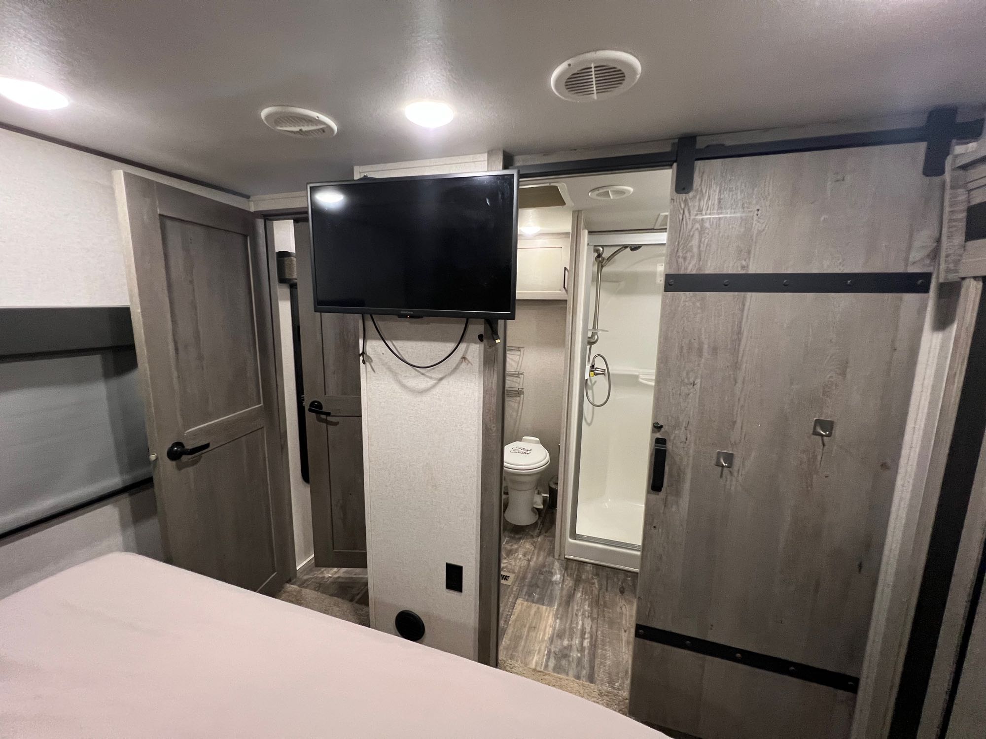 Inside a modern RV rental: bedroom with TV, leading to a bathroom with toilet & shower via a barn door.. Keystone RV Raptor Toy Hauler 2020