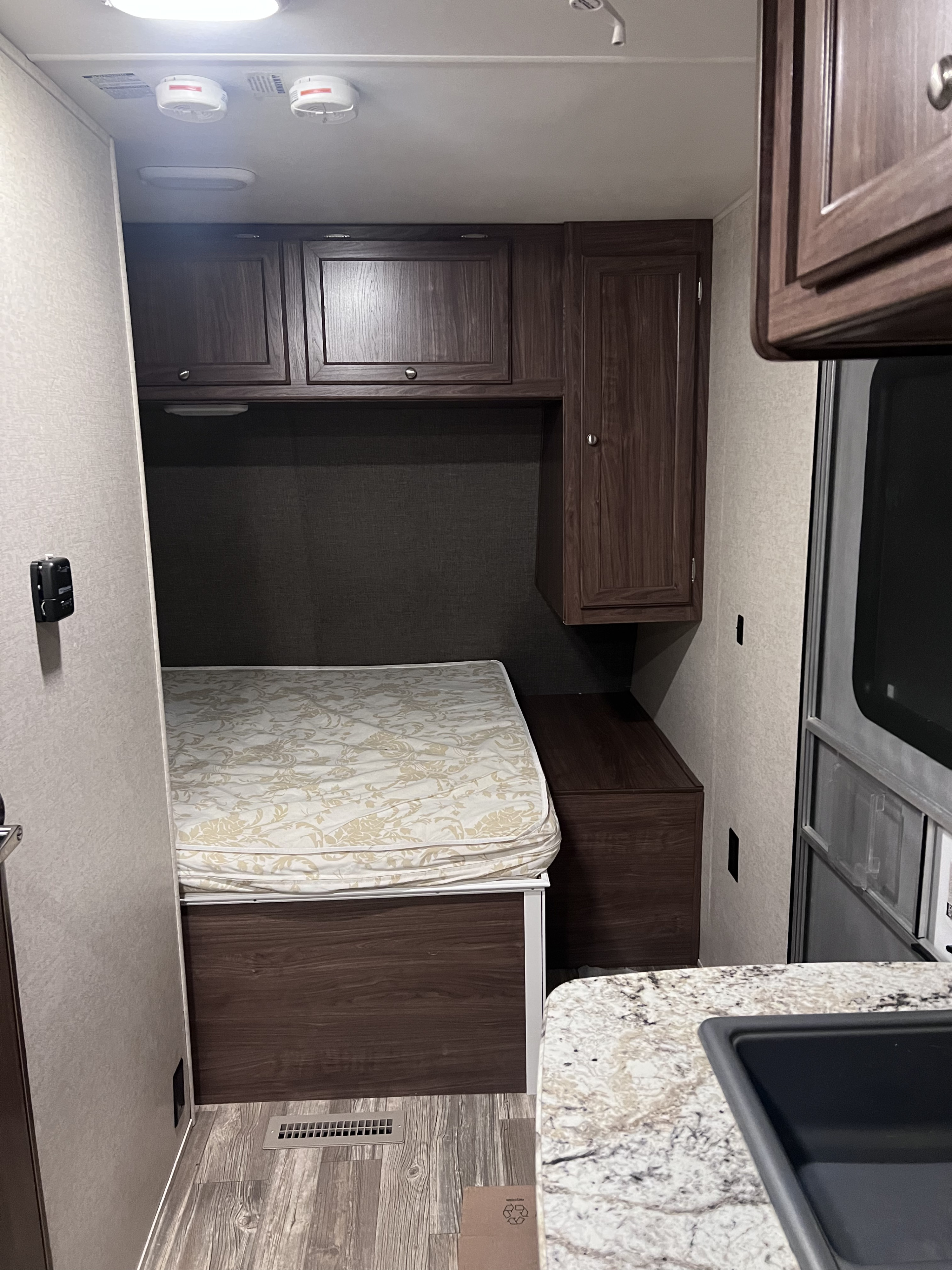 Cozy RV rental bedroom featuring a comfortable bed, built-in storage cabinets, and overhead safety devices.. Heartland RVs Pioneer 2016