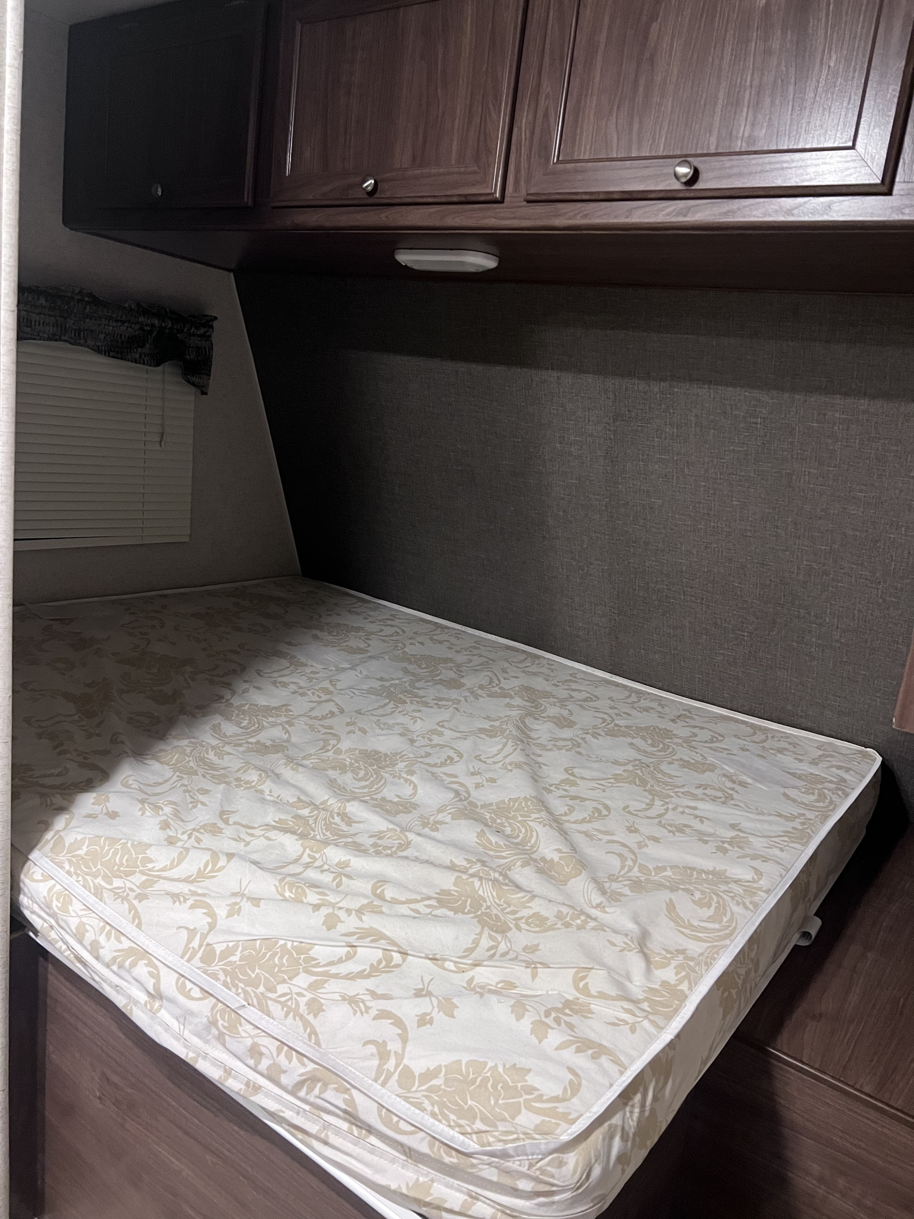 RV rental bed with white & tan floral mattress, dark wood cabinets, and window blinds. A cozy sleeping area for travel.. Heartland RVs Pioneer 2016
