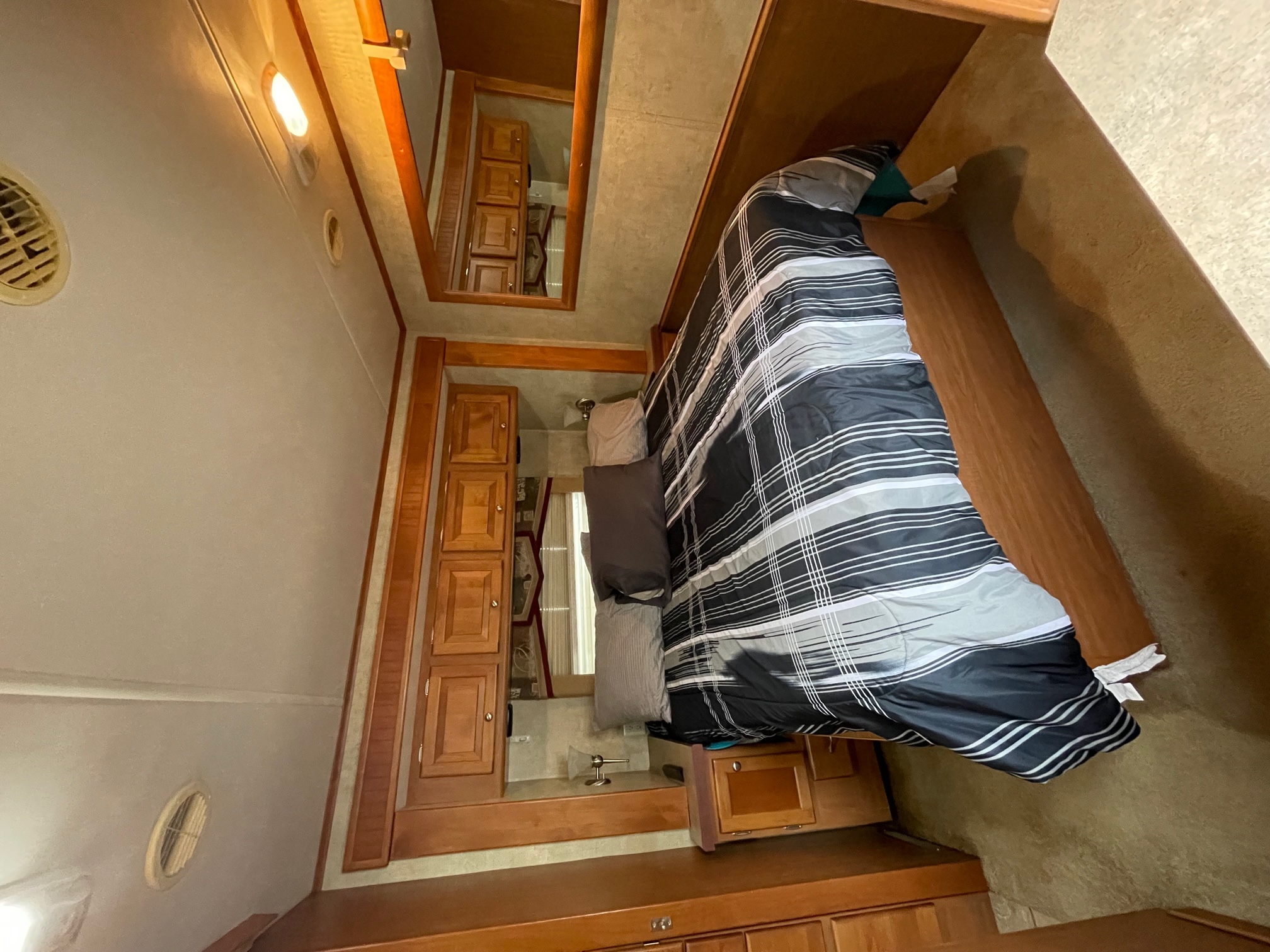 RV rental interior: A compact bedroom with a striped bed, wood cabinets, and ceiling vents, providing cozy accommodations.. Allegro Allegro Motorhome 2008