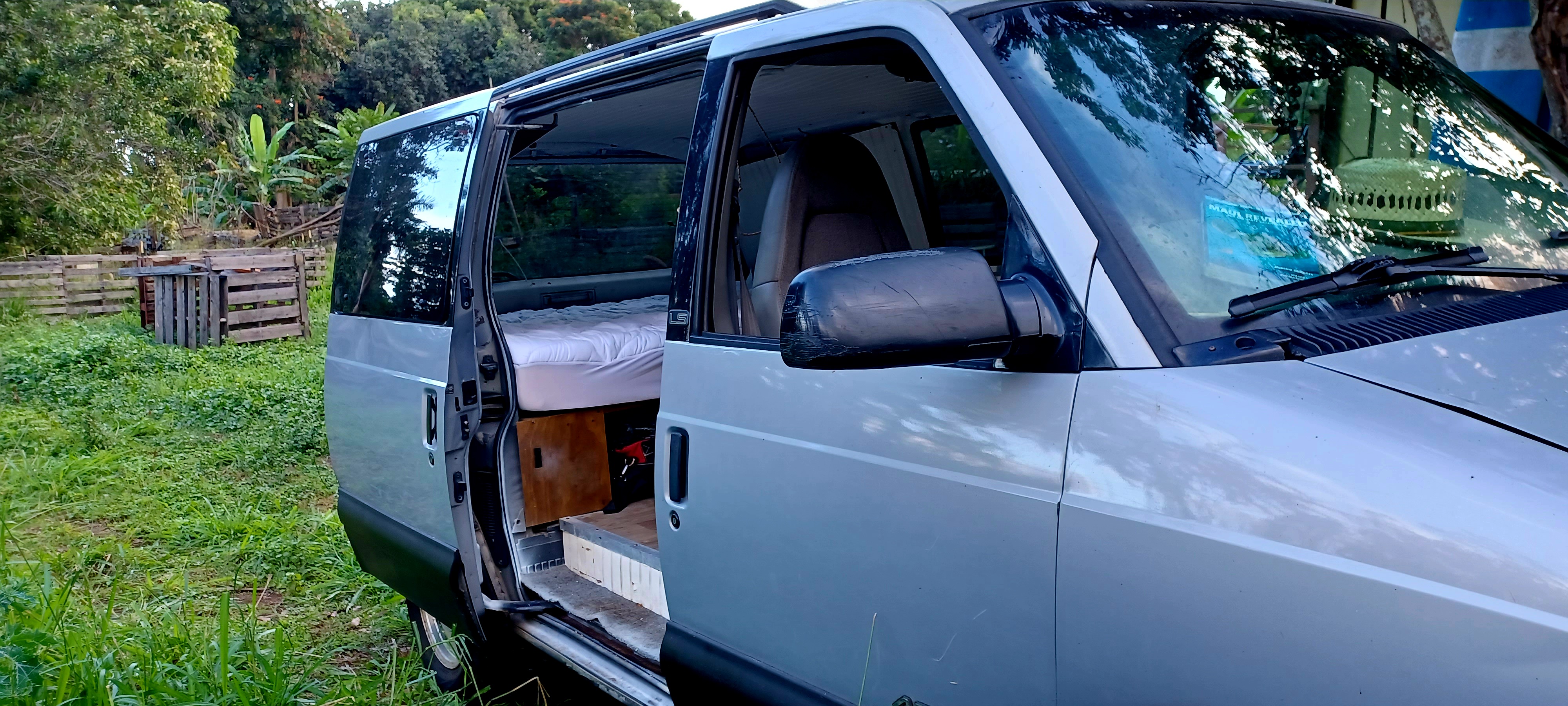 Converted van ready for your next rv rental adventure! Open doors reveal a cozy bed inside, parked in a lush outdoor setting.. Chevrolet Astro 2000