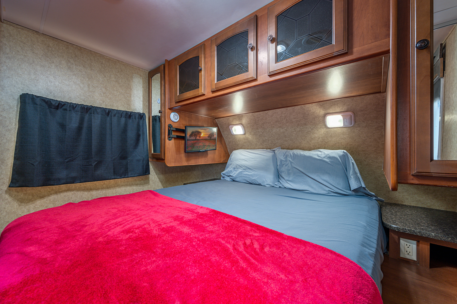 Comfortable RV rental bedroom with queen bed, overhead storage, TV, and convenient outlets for a cozy travel experience.. Heartland RVs North Trail 2013