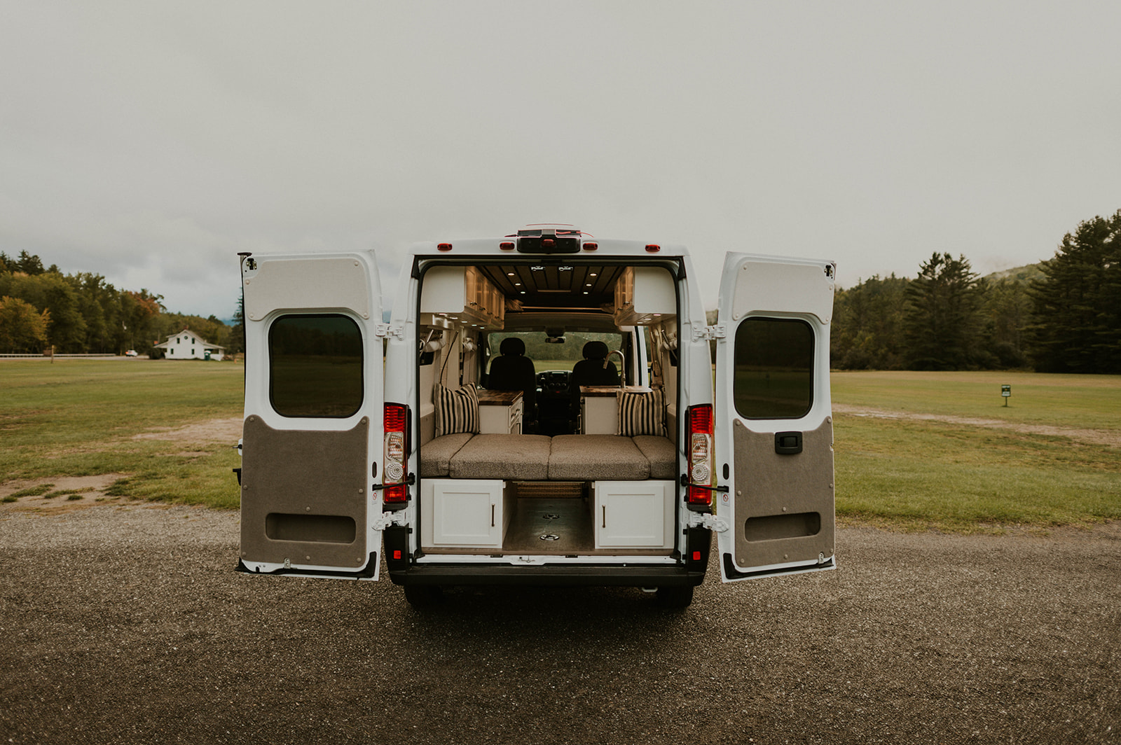 RV rental: Rear view of a white camper van with open doors, revealing a cozy, converted interior with bed and storage for van life travel.. Dodge Ram Promaster 2500 2021
