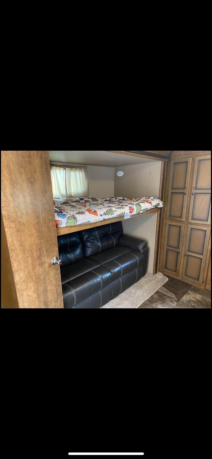 Cozy RV rental interior: colorful bunk bed above black leather sofa, with window and wood cabinets.. Crossroads RV Volante 2018