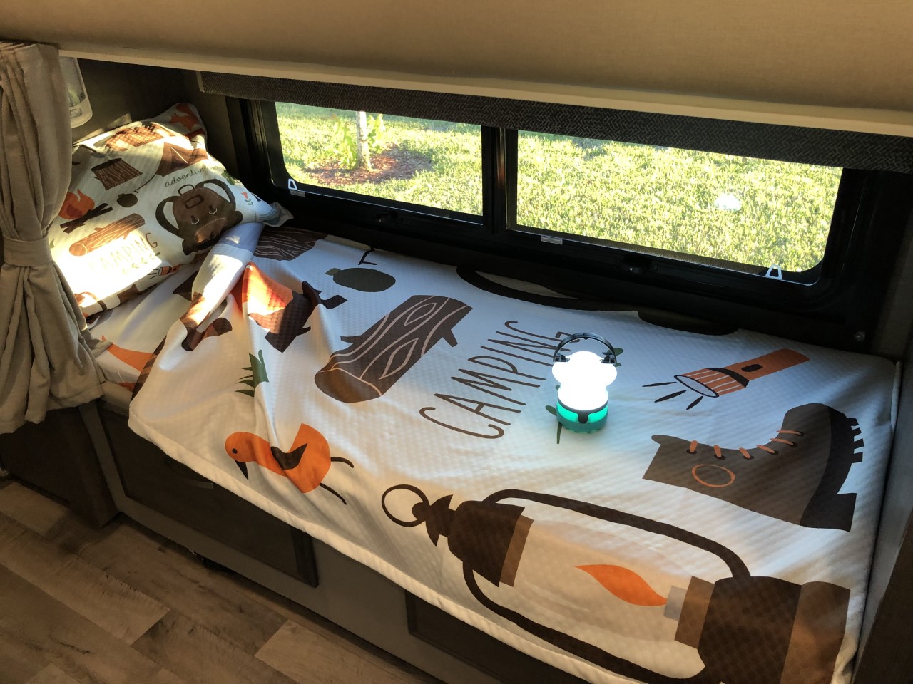 Inside an RV rental, a comfy camping-themed bunk bed features a glowing lantern and patterned bedding.. Jayco Redhawk 2023