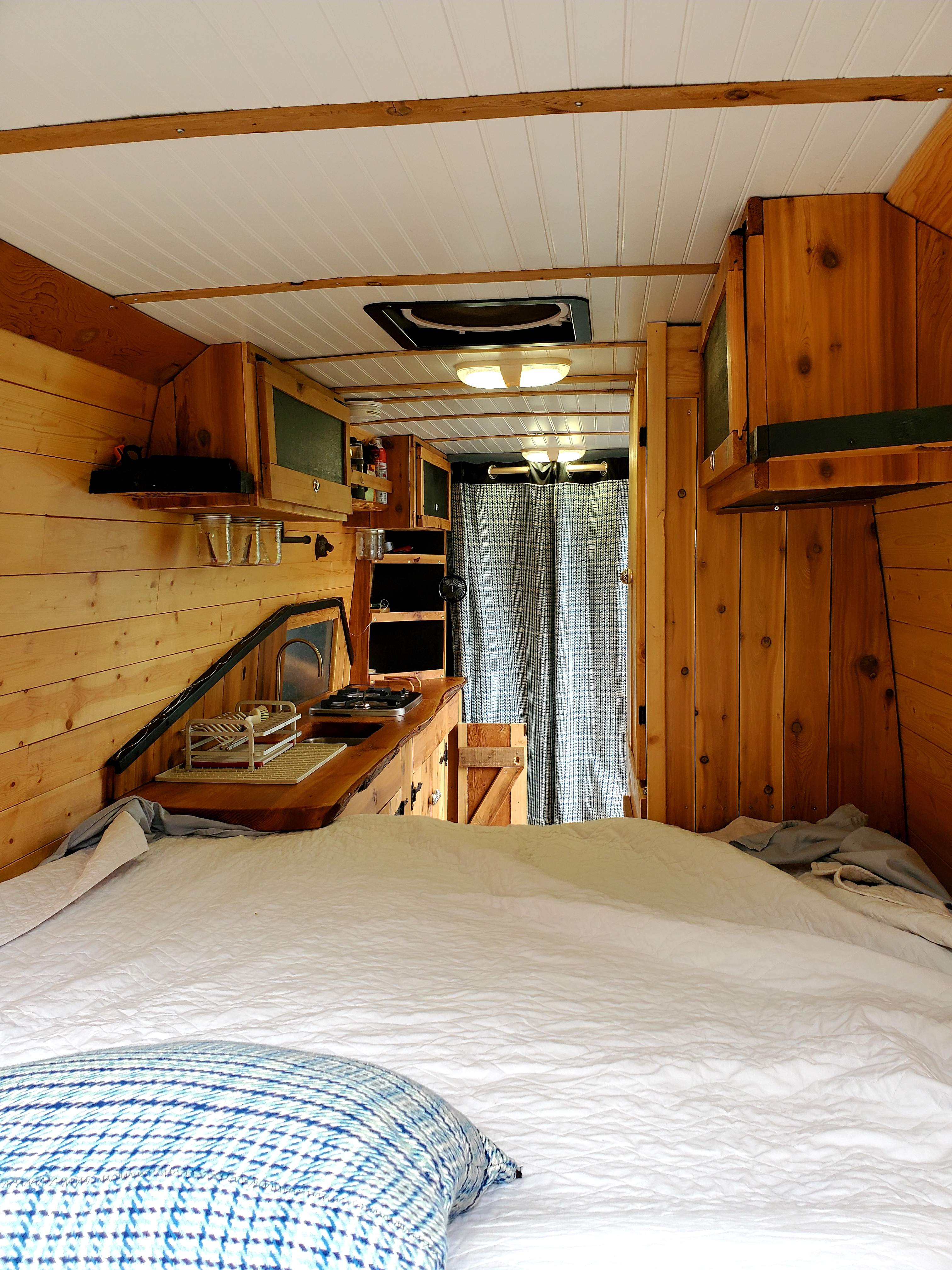 Cozy RV rental interior showing a comfortable bed, wooden walls, and a fully equipped kitchen with stove and sink.. Dodge Sprinter 2008