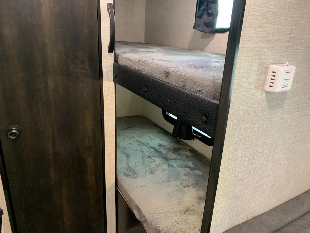 Inside an RV rental, two bunk beds provide compact sleeping. A dark wood door and window are also visible.. Jayco Jay Flight SLX 2022
