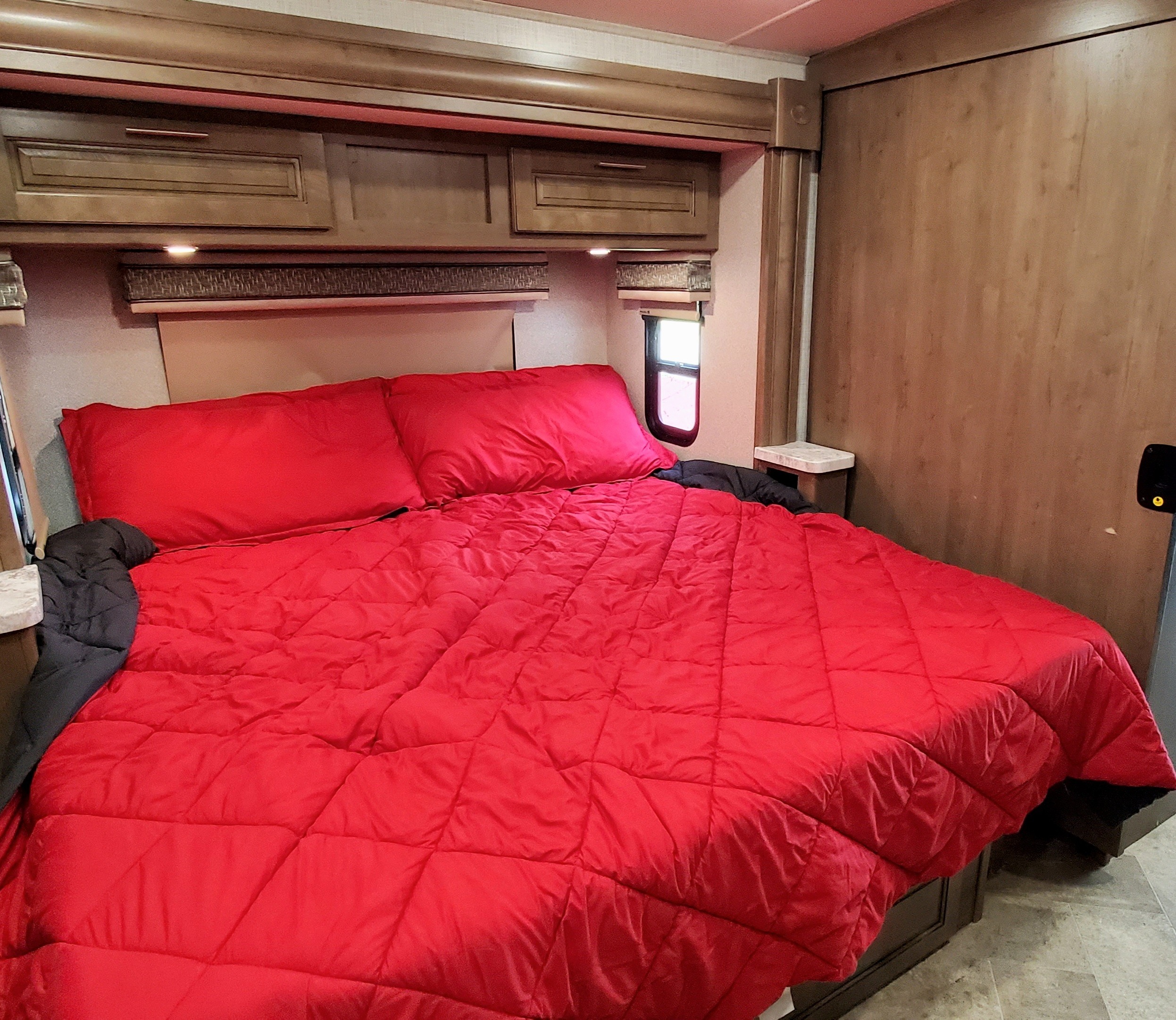 Spacious RV rental bedroom showcasing a queen-size bed with eye-catching red bedding, built-in cabinetry, and bedside conveniences.. Georgetown GT5 2019