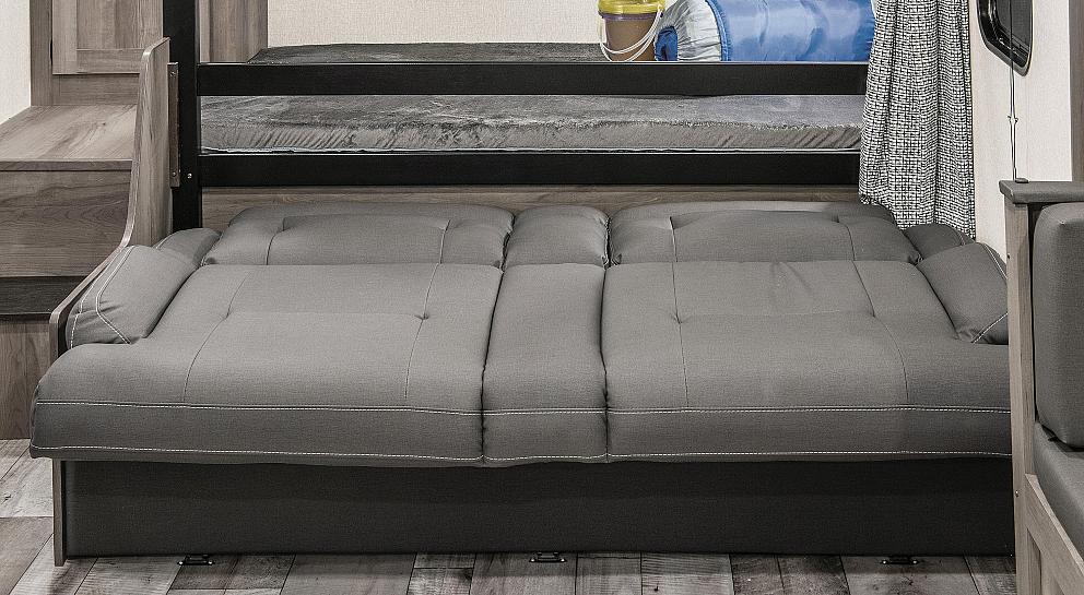 This RV rental's versatile interior features a gray multi-section sofa extended below bunk beds, creating a flexible sleeping and lounging area.. Sportsmen SE 2021