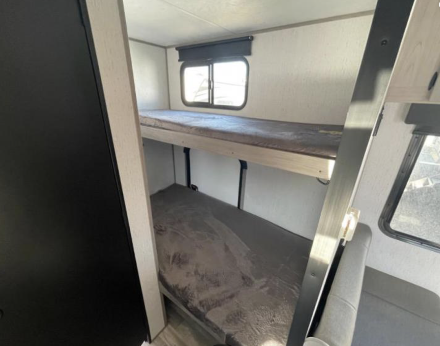RV rental interior showing compact sleeping area with two bunk beds, mattresses, and windows. Ideal for family travel.. Dutchmen Kodiak Cub 175BH 2022