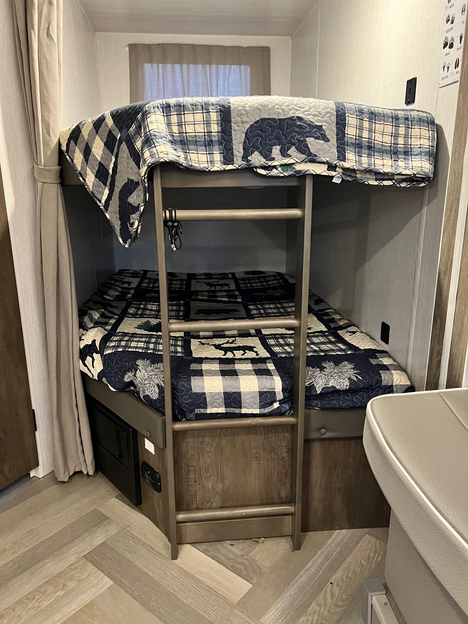 Inside an RV rental: a comfortable bunk bed sleeping area with themed quilts, a ladder, and privacy curtains.. Forest River Wildwood X-Lite 2022