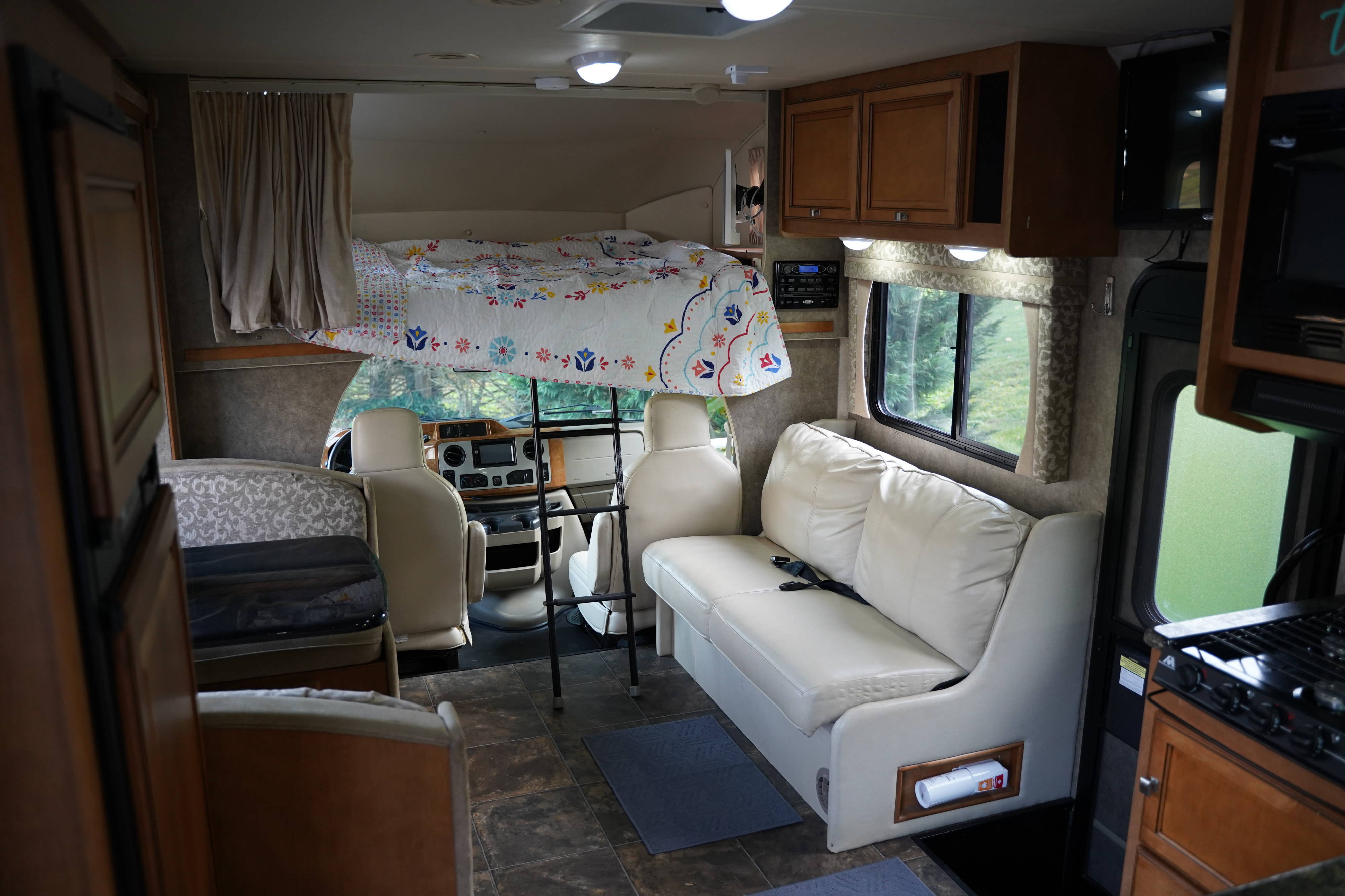 Explore this bright RV rental interior featuring a cozy overhead bed, ample seating, and a functional kitchen.. Itasca Impulse 2013