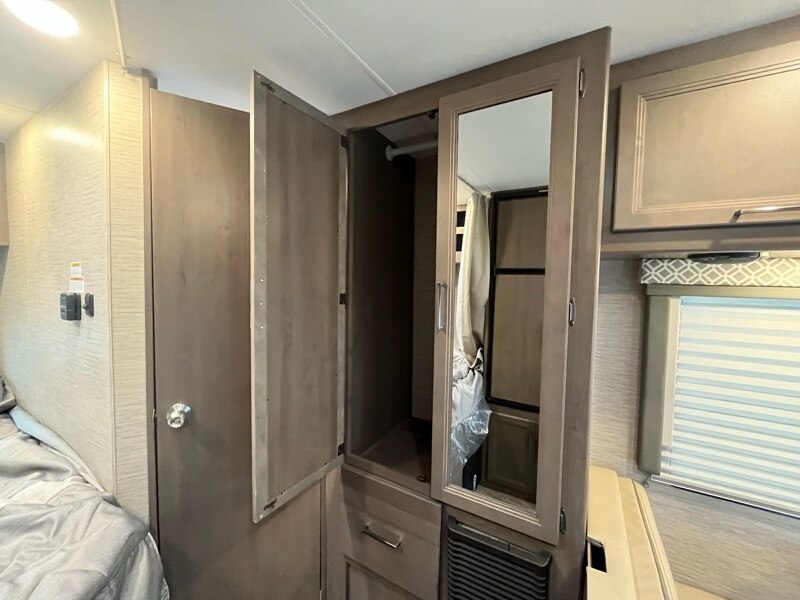 RV rental interior: Bedroom area with open wardrobe, full-length mirror, and window with blinds.. Thor Motor Coach Four Winds 2023