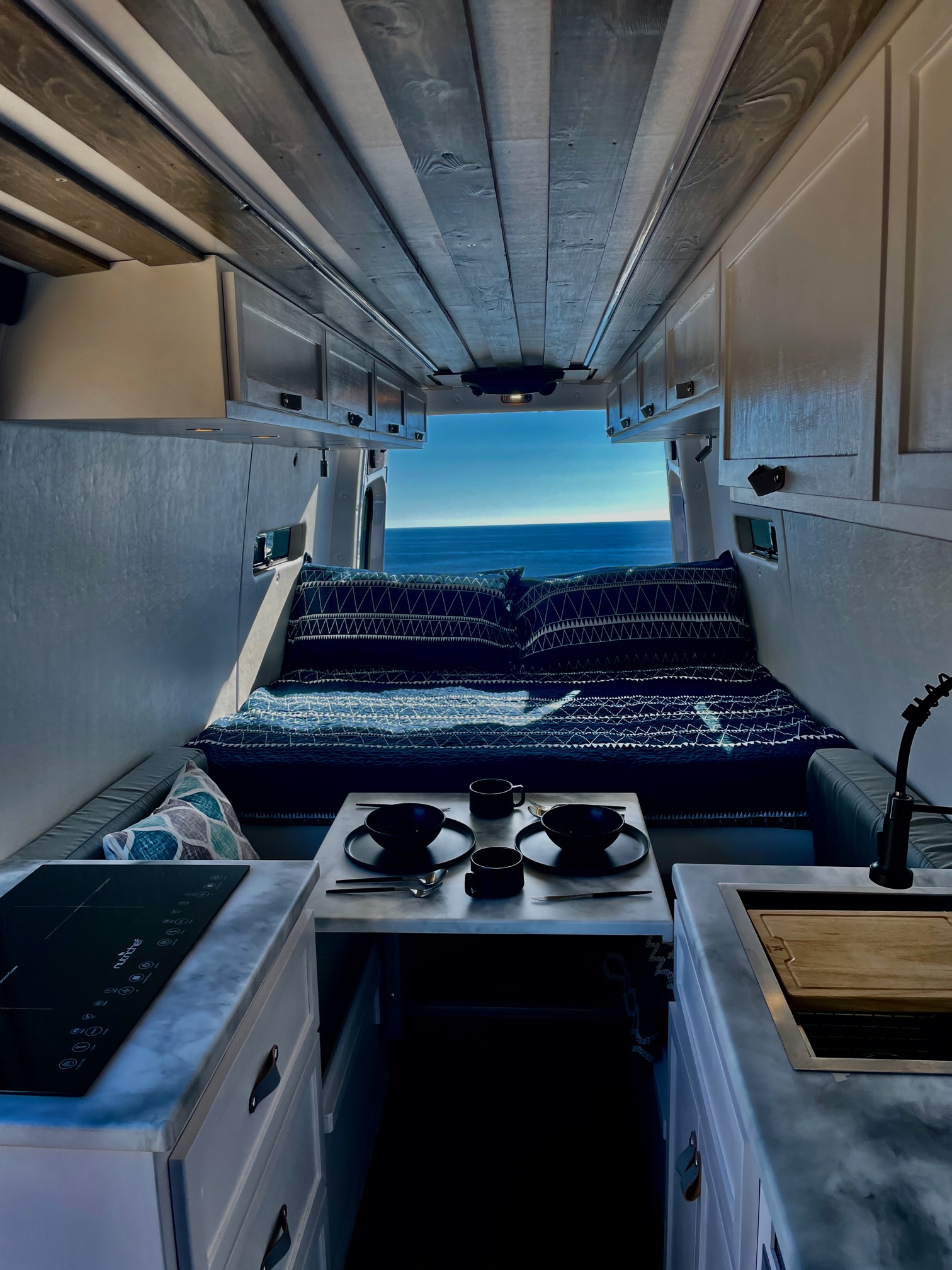 Cozy RV rental interior with ocean view bed, kitchen, and dining area. Perfect for van life adventures.. Mercedes-Benz Sprinter 2022