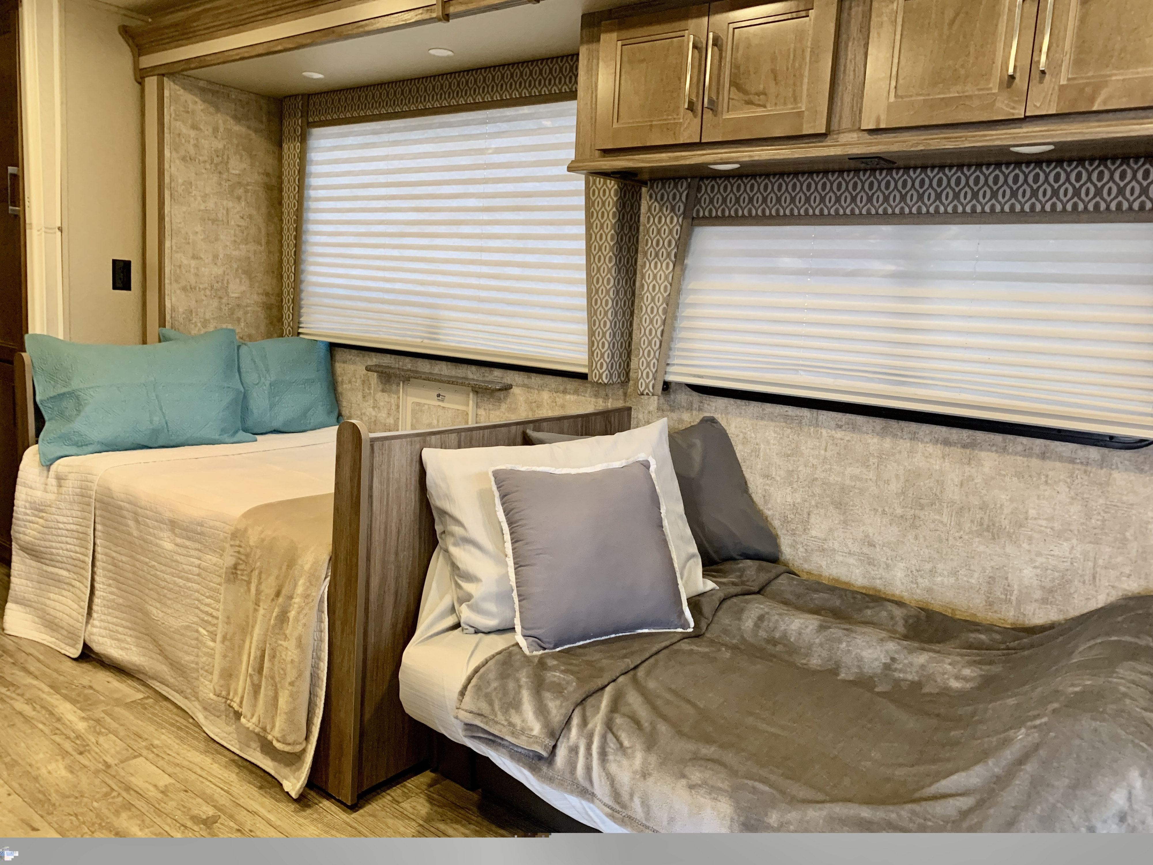 Cozy RV rental bedroom featuring two comfortable beds, one with blue and one with gray bedding, amidst wood and neutral interior.. Jayco Envoy 100 2018