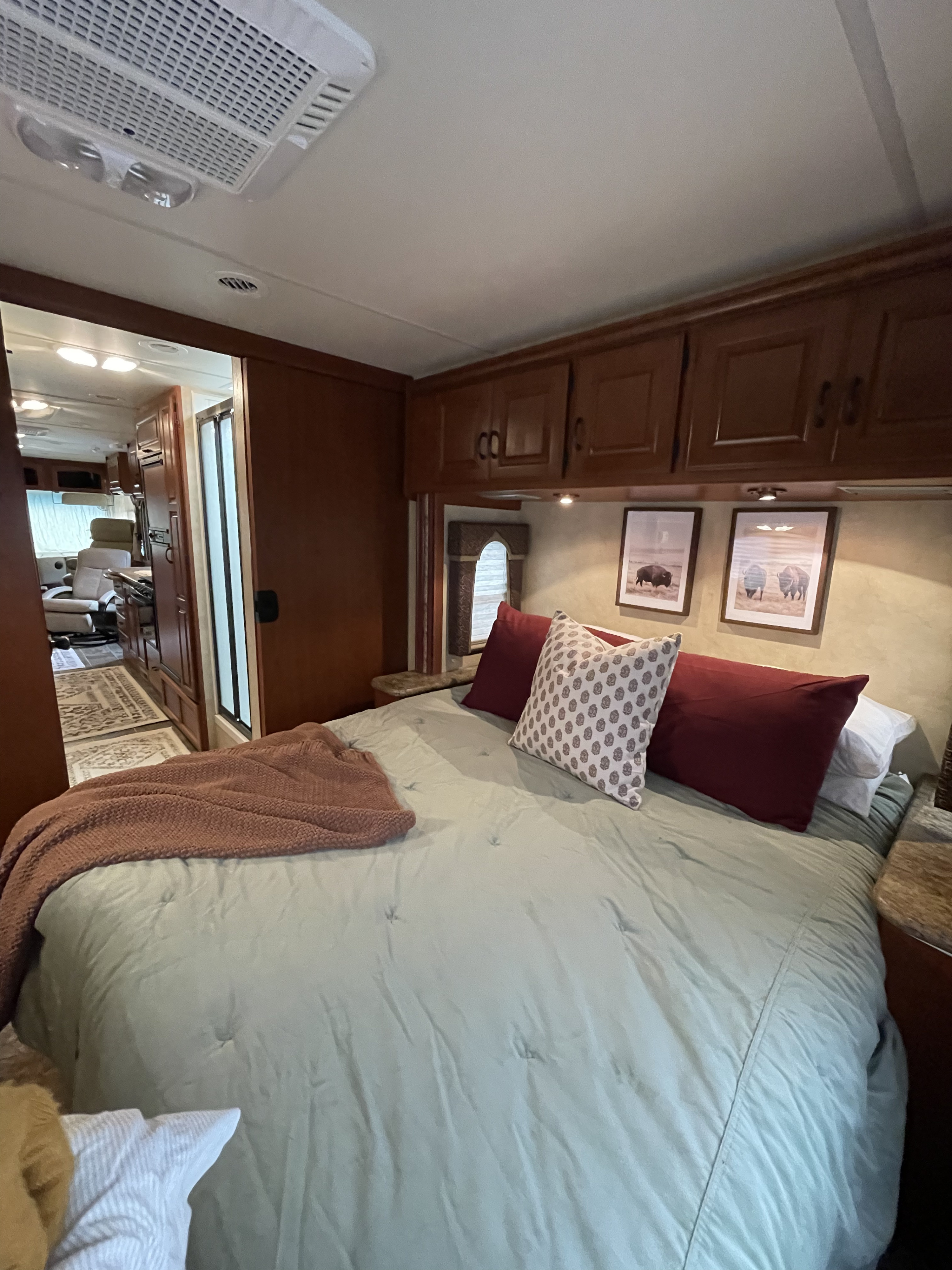 Comfortable RV rental bedroom featuring a bed with green bedding, bison artwork, and a view into the spacious living area.. Thor Hurricane 2012