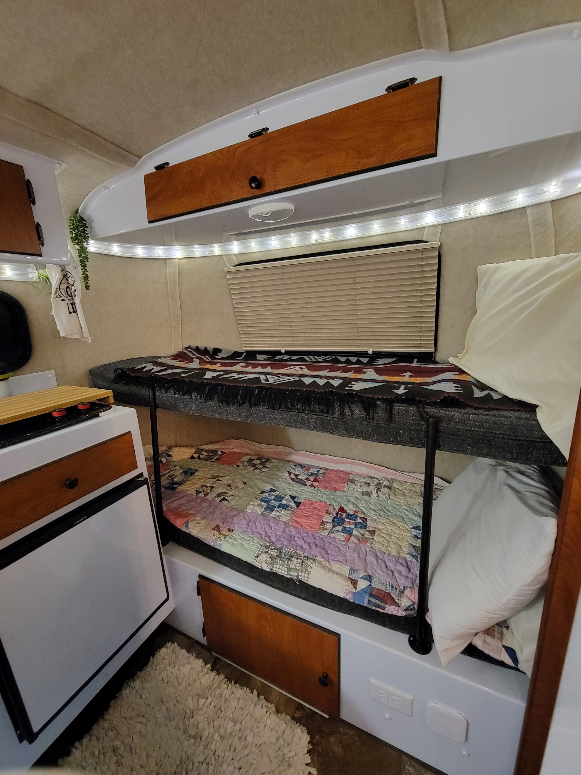 Experience an RV rental: a compact interior featuring cozy bunk beds, a small kitchen, and warm string lights.. Scamp Trailer 2022