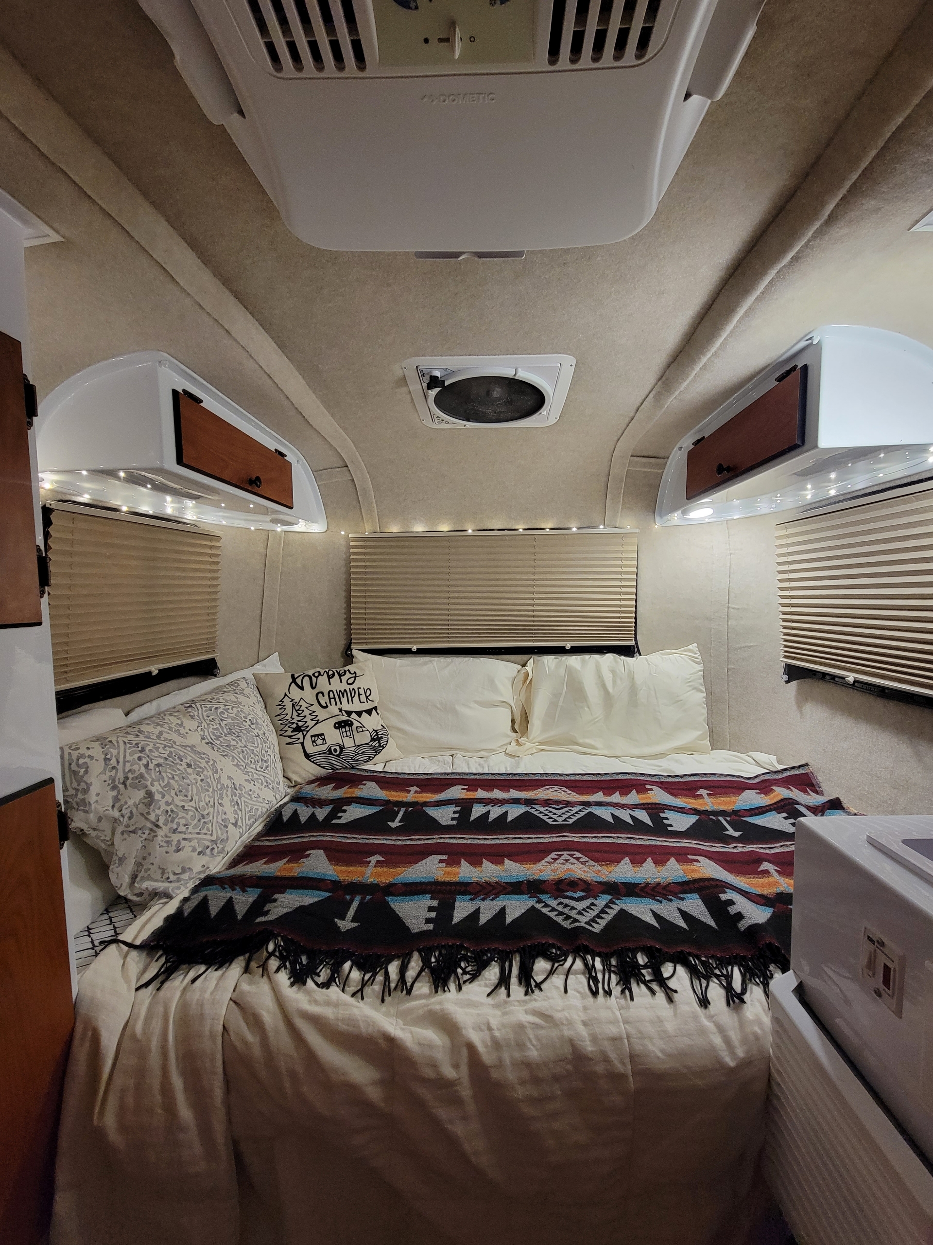 Cozy RV rental bedroom with a patterned blanket, Dometic AC, and warm lights, ready for your next adventure.. Scamp Trailer 2022