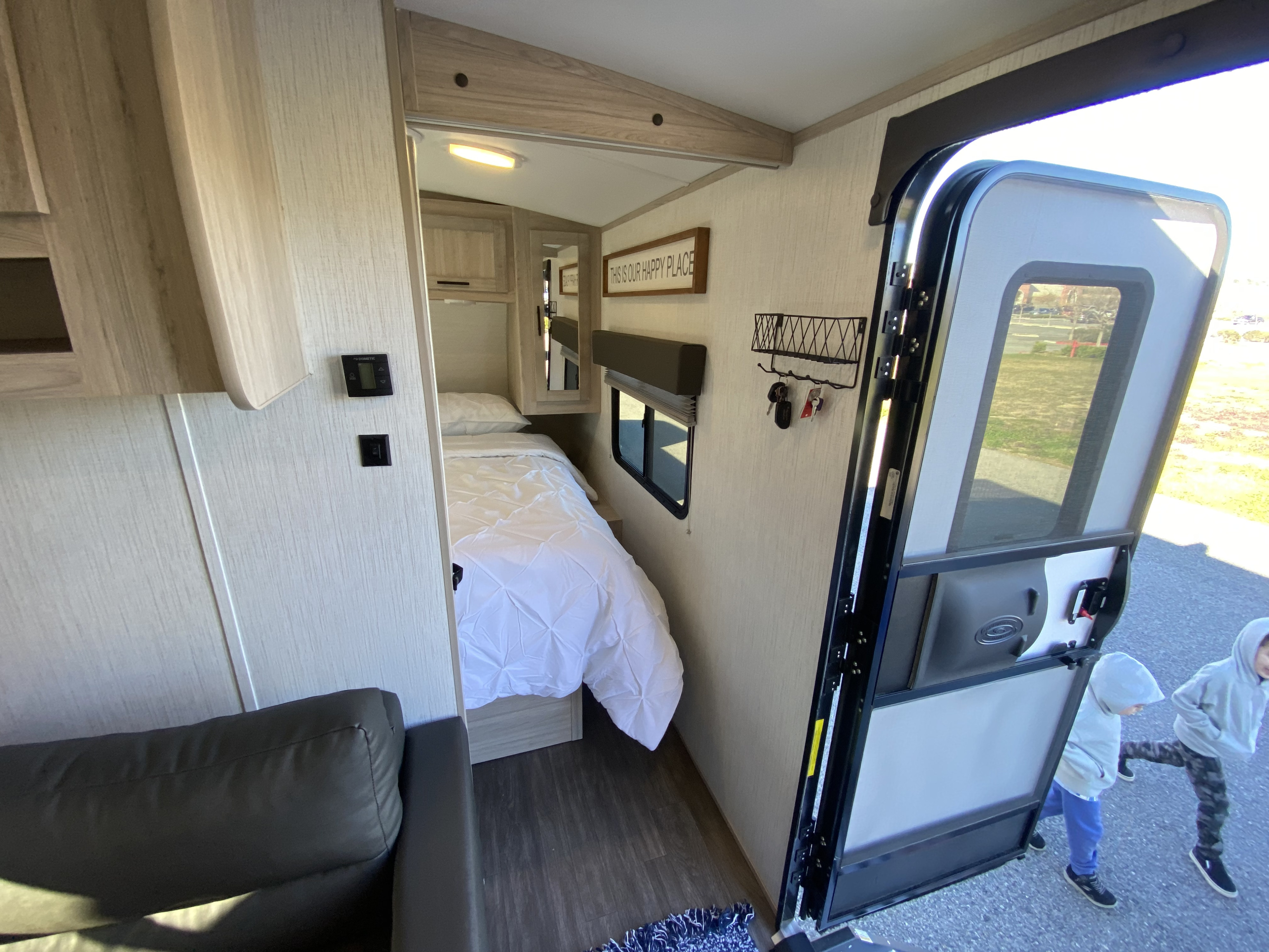Inside a modern rv rental with a cozy bedroom, sofa, and open door. Kids seen playing outside.. Cruiser RV Shadow Cruiser 2022