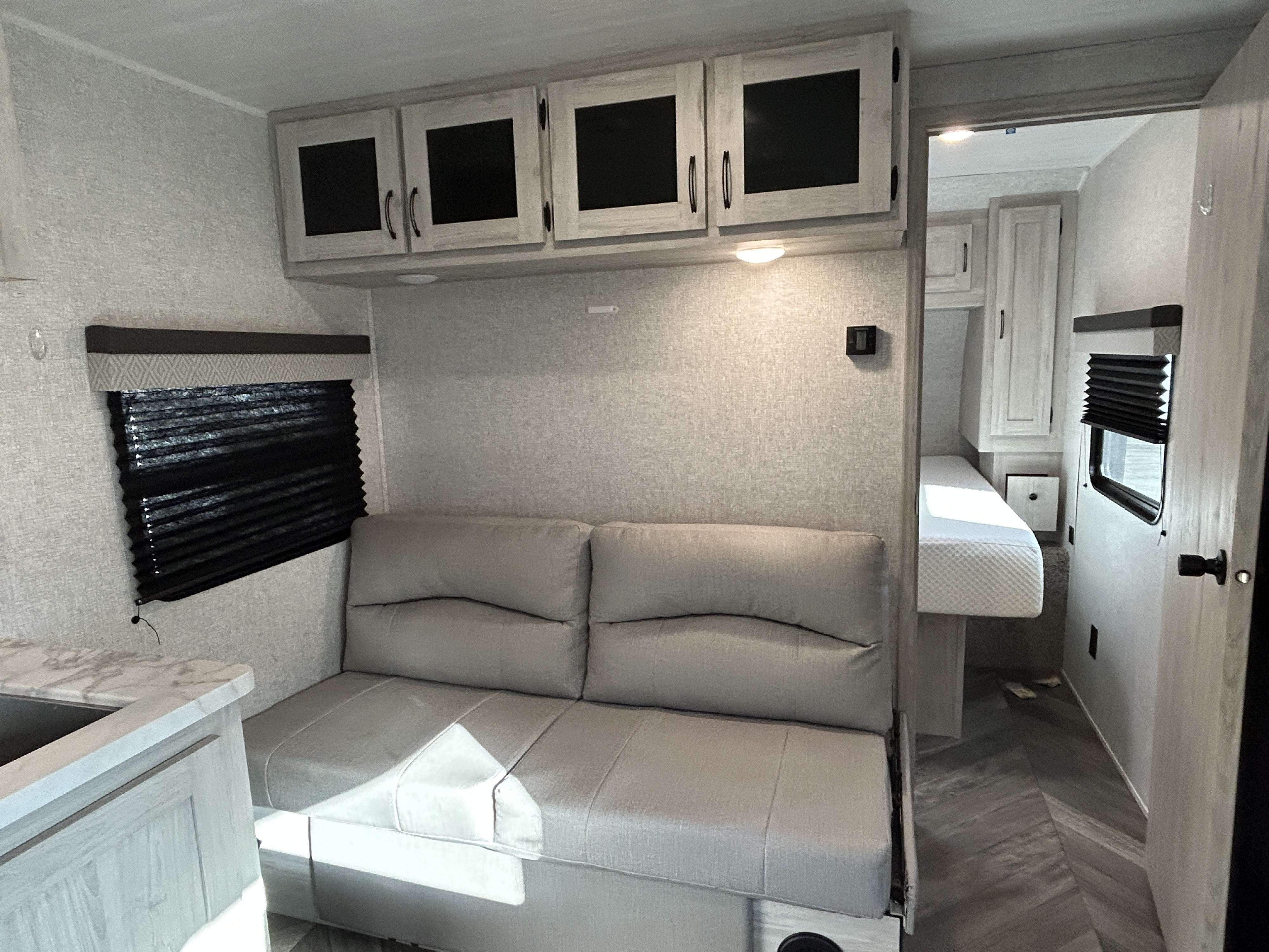 RV rental interior: light-colored walls, a sofa, overhead cabinets, window with blinds, and bedroom.. East to West Della Terra 2022