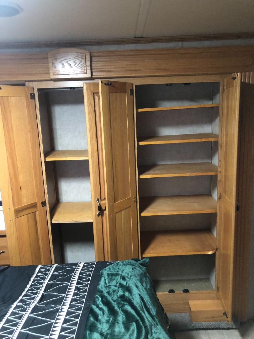 RV rental bedroom storage: open wooden cabinets with shelves and a bed. Compact and functional space for your trip.. Holiday Rambler Ambassador 2005