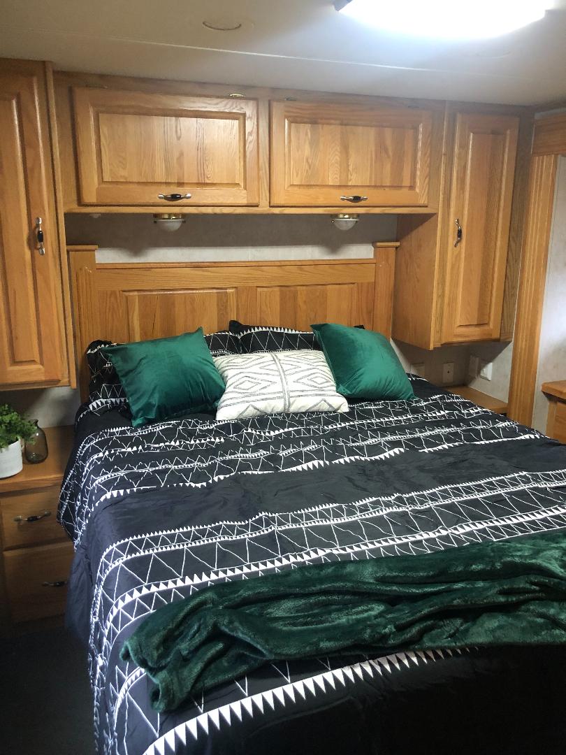 Cozy RV rental bedroom features geometric bedding, green pillows, and warm wooden cabinets.. Holiday Rambler Ambassador 2005