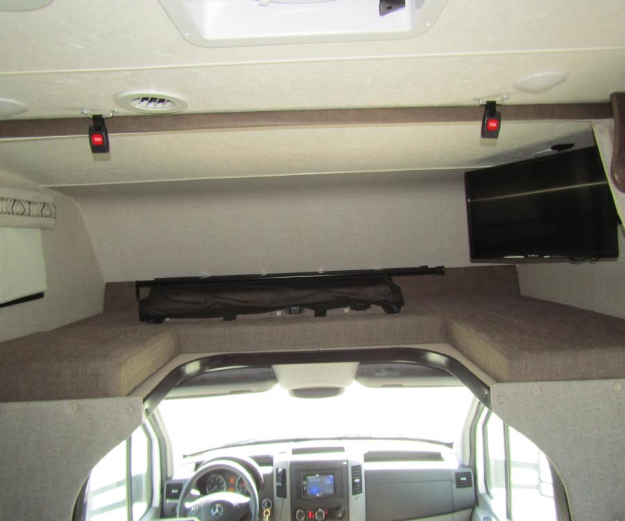 Spacious cab-over bunk in an RV rental, featuring a TV, safety net, and comfortable sleeping area.. Coachmen Prism 2020