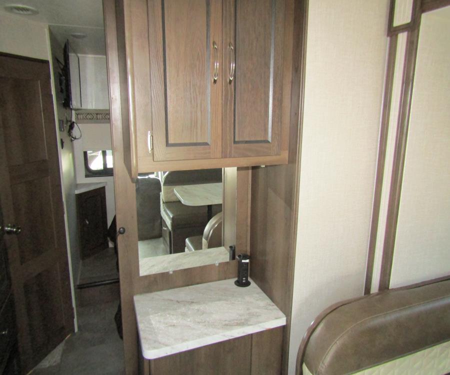 RV rental interior: wooden cabinetry, a countertop with an outlet, and a mirror reflecting the dinette and bed.. Coachmen Prism 2020