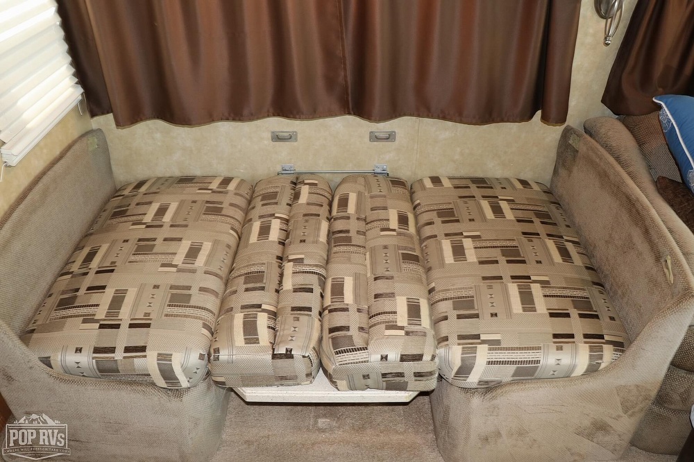 RV rental dinette converted to a bed, featuring patterned cushions and brown curtains. A functional RV interior.. Georgetown XL 2006