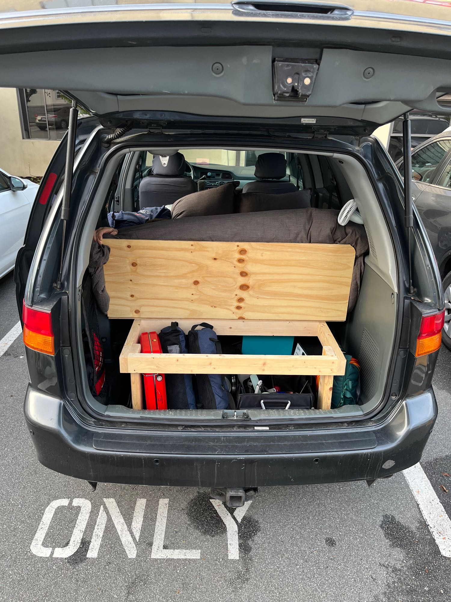 Back of a dark minivan with a custom wooden bed platform & storage. Ideal for van life, road trips, or an RV rental alternative.. Honda Odyssey 2003