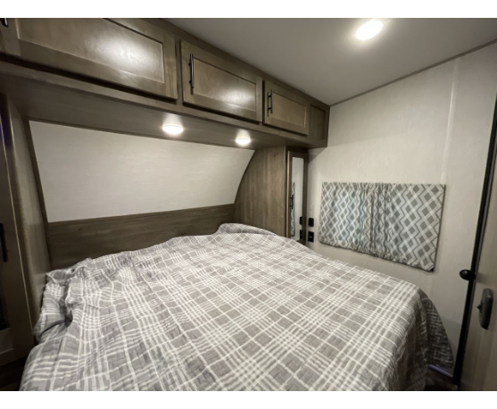 Step into comfort! This RV rental bedroom features a comfy bed, overhead cabinets, and a window with patterned curtains.. Forest River Cherokee Wolf Pack 2022
