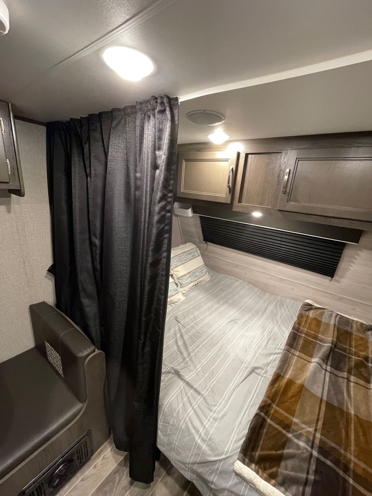 Cozy RV rental interior: a partitioned bedroom with bed, plaid blanket, and overhead cabinets, beside a small seating area.. Jayco Jay Flight SLX 2021