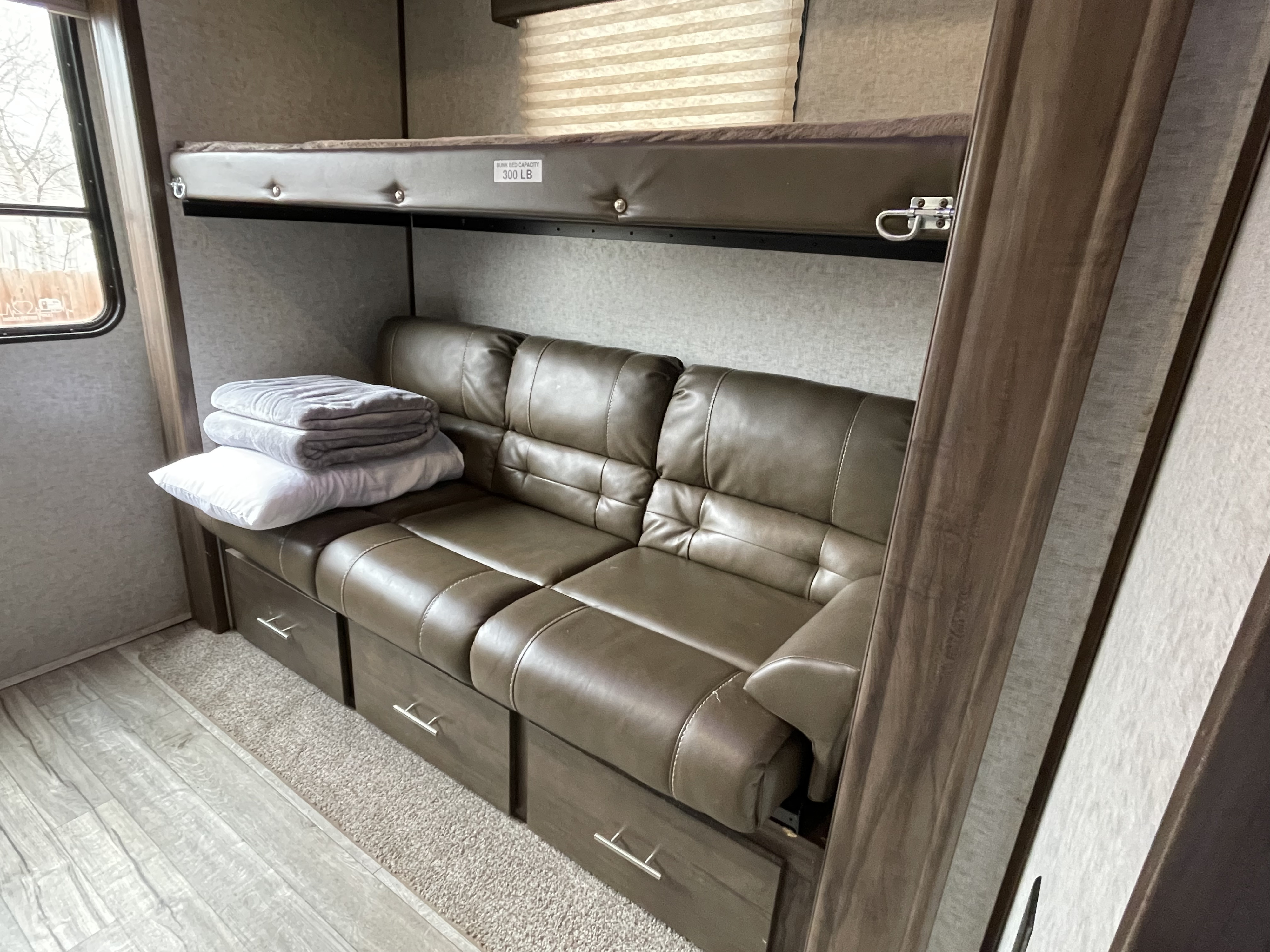 Cozy RV rental interior showcasing a bunk bed (300lb capacity) over a sofa with built-in storage drawers, ideal for family trips.. Forest River Cherokee Arctic Wolf 2018