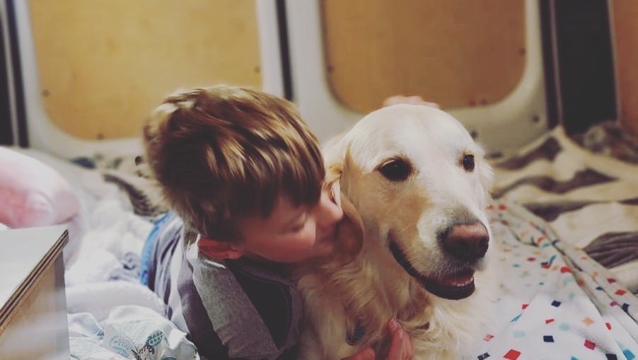 Cozy RV rental moments: A child shares a loving hug with their golden retriever inside a comfortable RV.. RAM ProMaster 2022